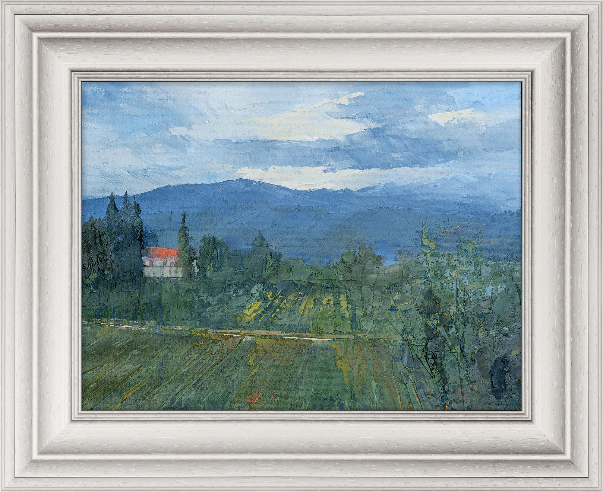 Distant Mountains, an original oil painting by Paul Kenton in a white ornate frame: blue mountains beneath a cloudy sky, with a small red-roofed house among green fields and cypresses.