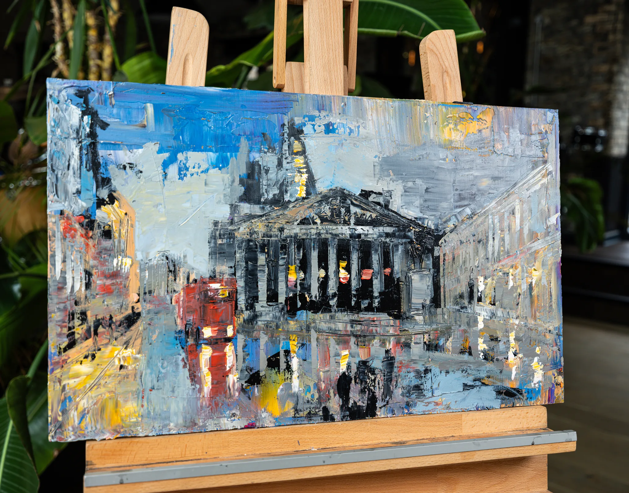 Bank Junction, an original painting by Paul Kenton on a wooden easel: a columned building, red bus and glowing wet street at dusk.