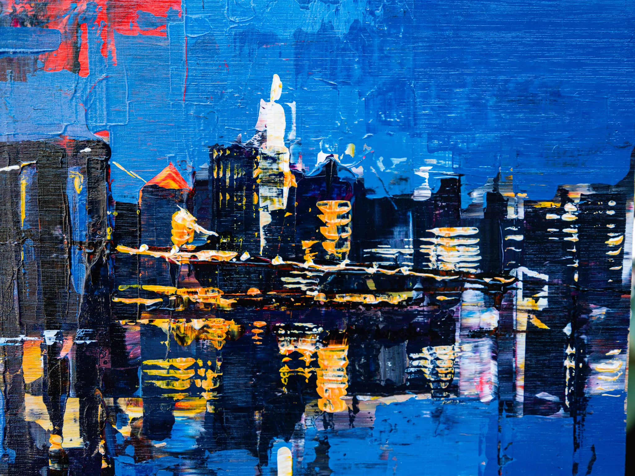 Close-up of City After Dark, an original painting by Paul Kenton: thick blue and black brushwork shows a night skyline with glowing gold windows reflected in dark water.