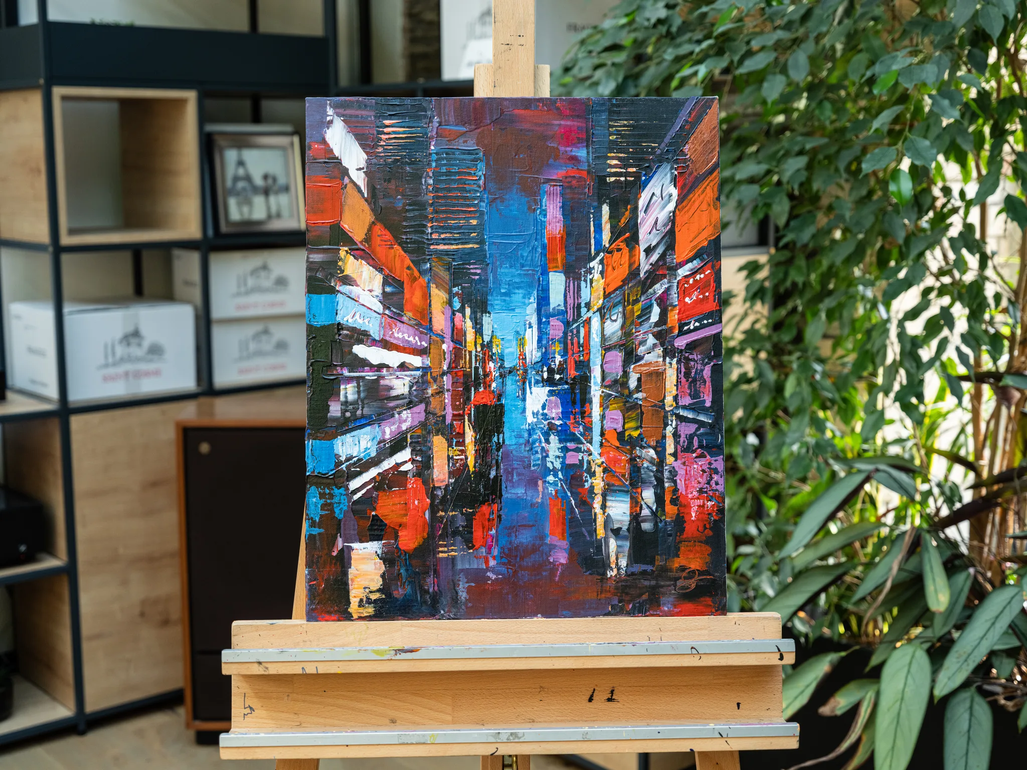 City Corridor, an original painting by Paul Kenton, on an easel in a studio: a narrow New York street of glowing red, orange and blue buildings, thickly textured.
