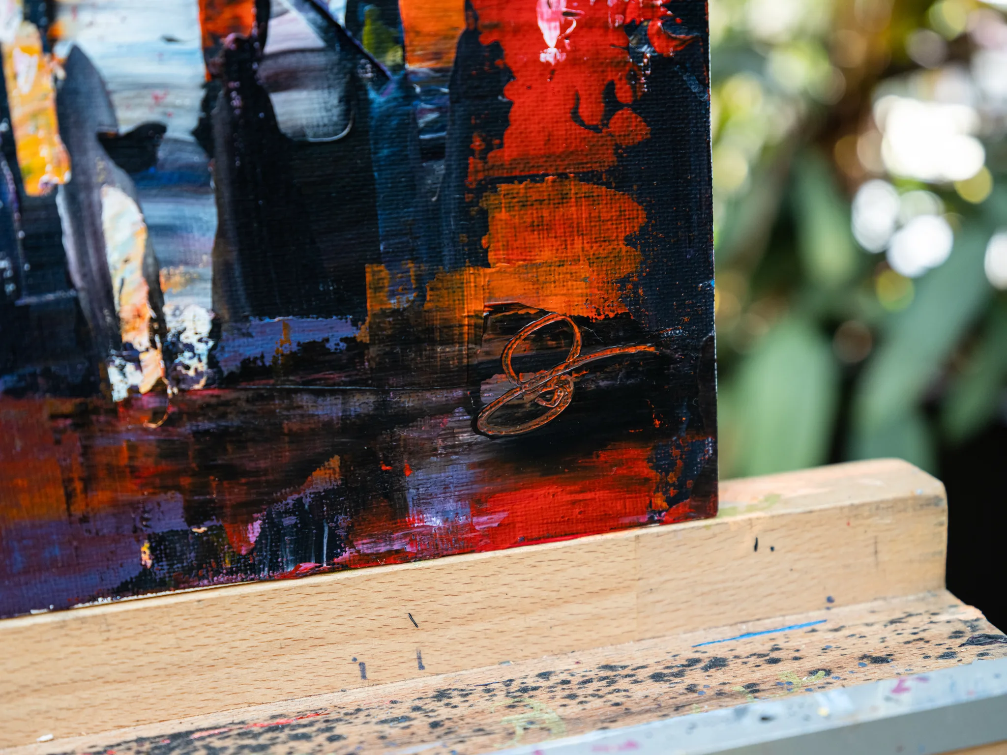 Close-up of City Corridor, an original painting by Paul Kenton, showing thick red, orange and black impasto brushwork and a looping metallic gold signature on a wooden easel ledge.