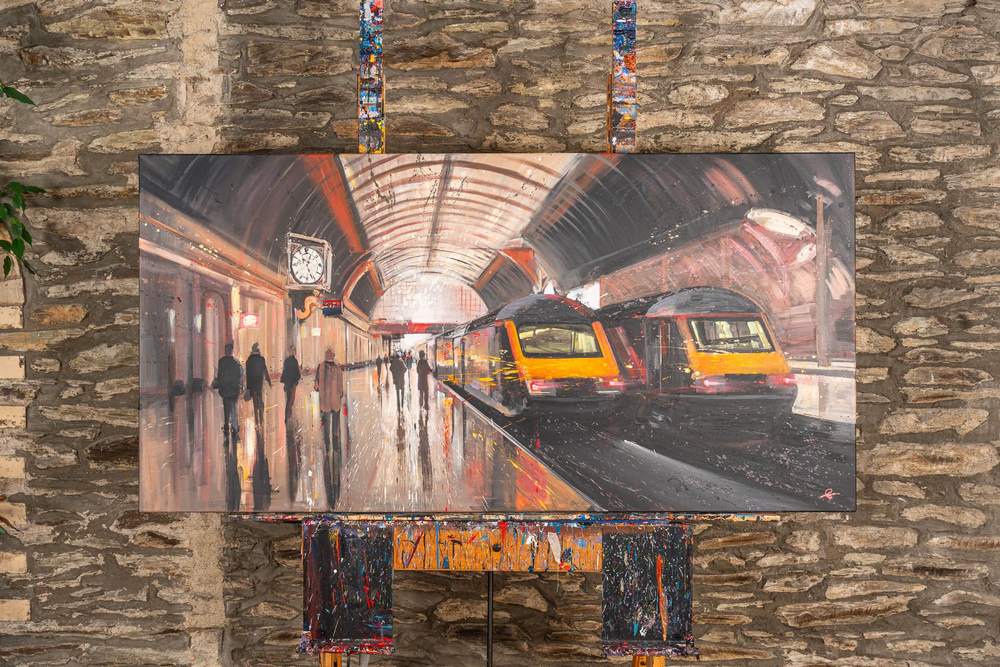 Capital Connections, an original oil painting by Paul Kenton, hangs on a stone wall, showing a blurred platform with commuters and two yellow-fronted trains under a curved roof.