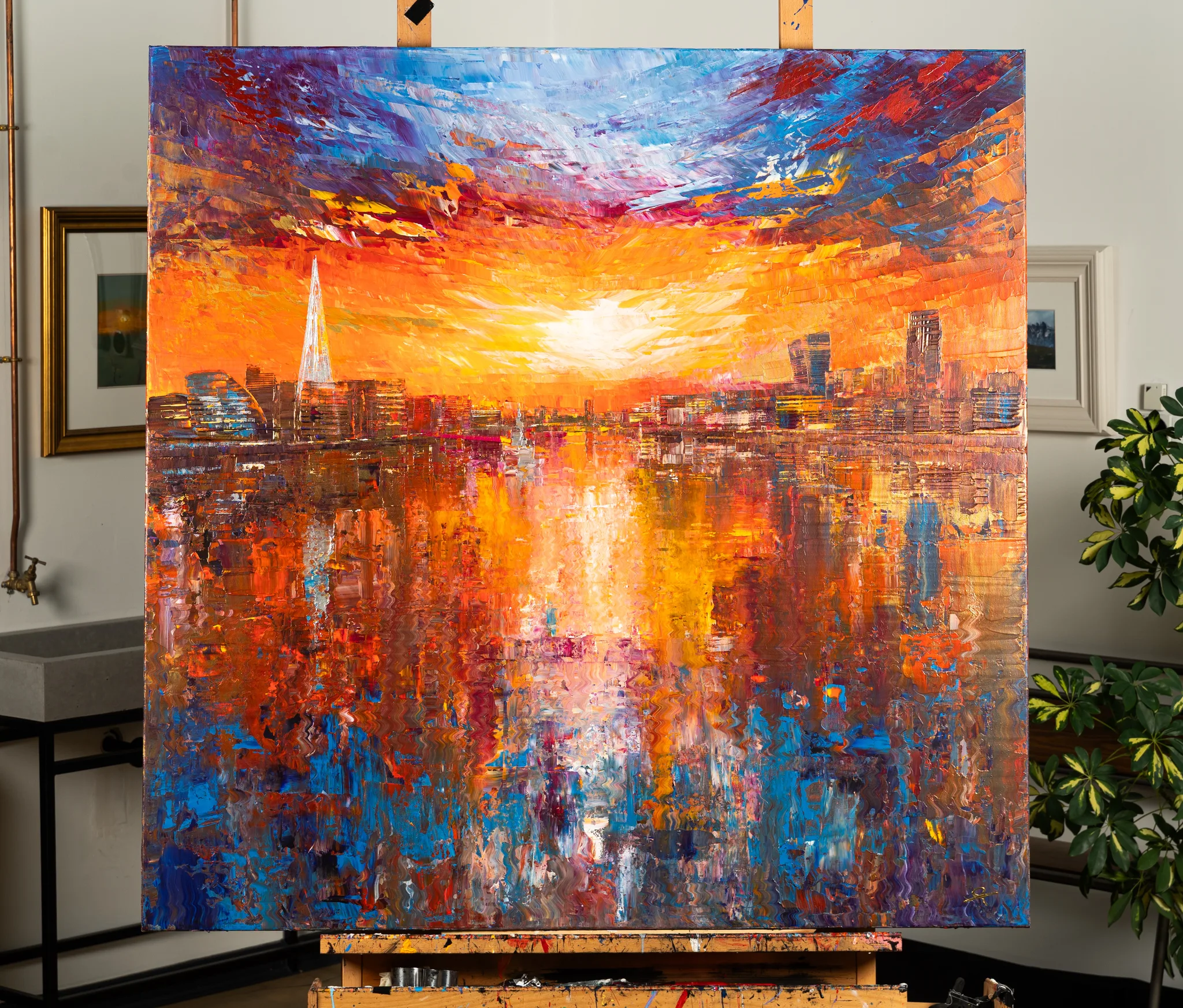 Currents of Light, an original painting by Paul Kenton, on an easel in a studio: a bold sunset over a London skyline with the Shard, and warm orange and blue reflections rippling across the river.