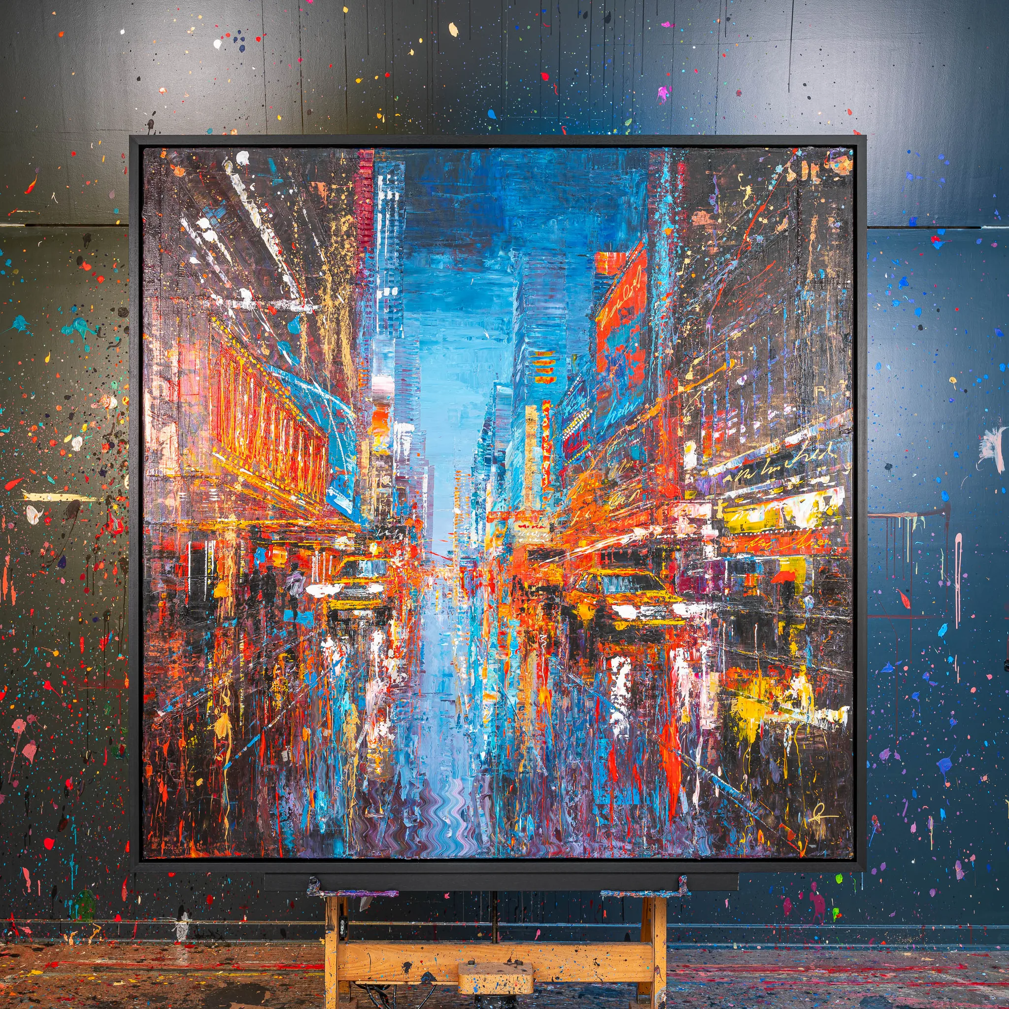 Empire City Spectrum, an original painting by Paul Kenton, hangs in a dark studio on an easel. Its bold, textured New York street scene glows with orange, red and blue neon above yellow taxis.