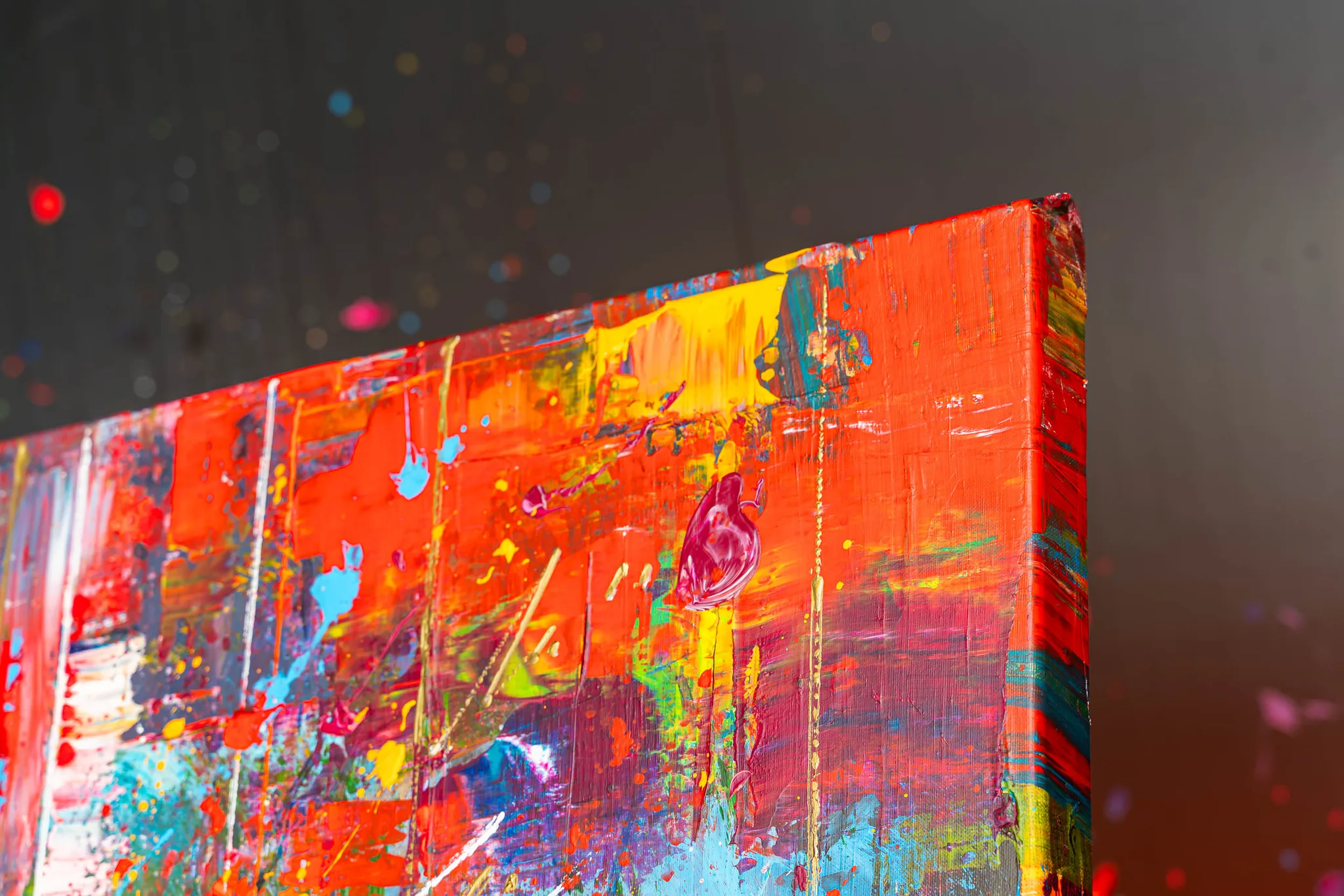 Close-up of the corner of Fairytale Of New York, an original mixed media painting by Paul Kenton, showing bold red, orange and yellow strokes, drips and splatters of blue and pink, and thick textured paint on the canvas edge.