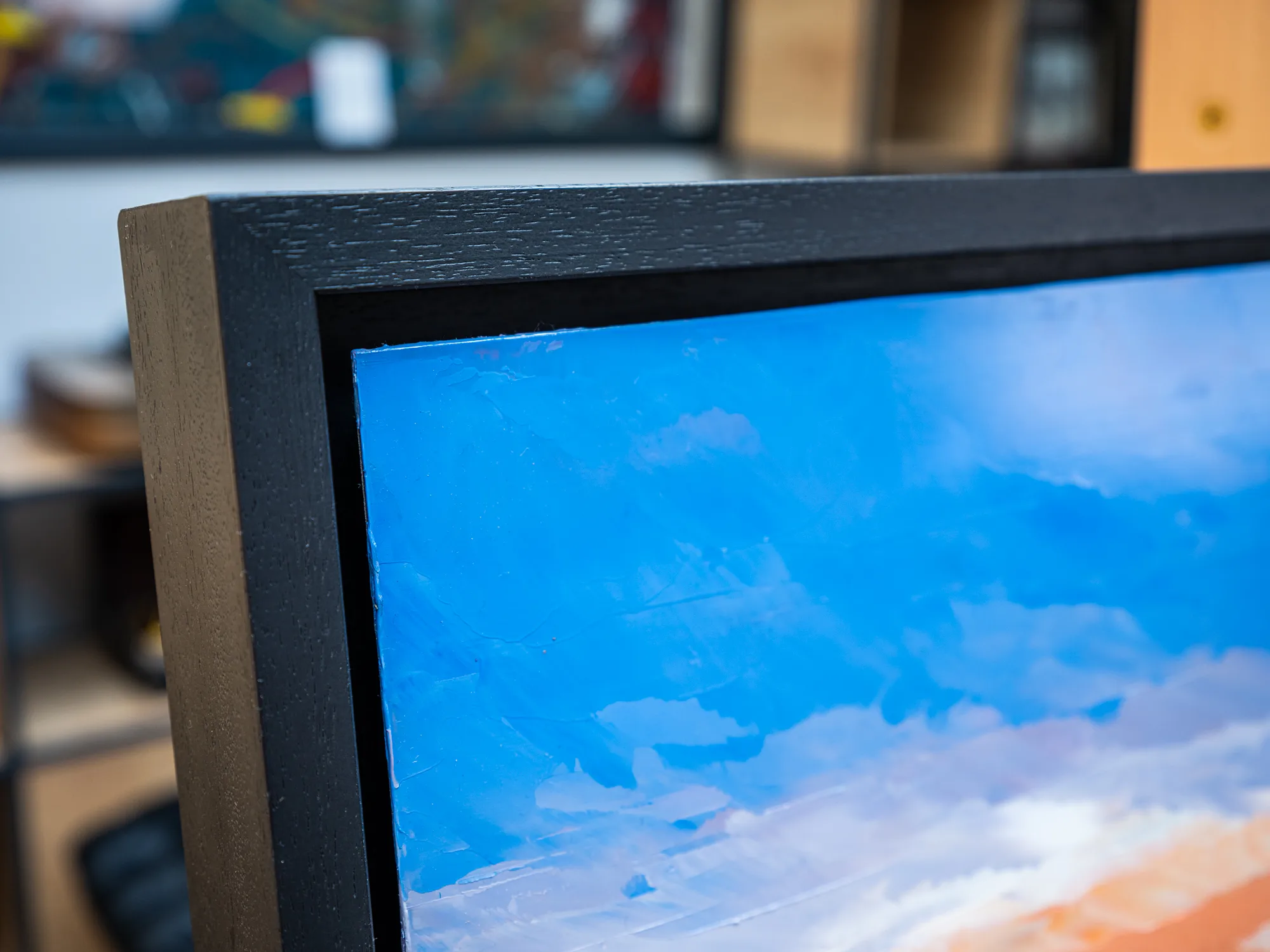 Close-up of Golden Capital, an original oil on aluminium painting by Paul Kenton, showing thick, textured brushwork in blue sky fading to pale clouds and warm orange at the lower edge, within a dark wooden frame.