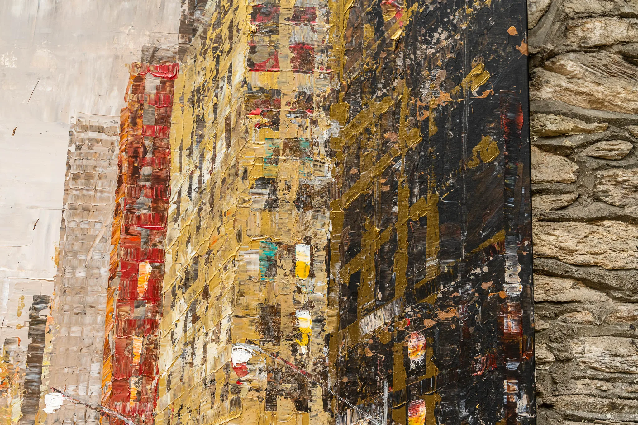 Close-up of Golden Metropolis, an original mixed media painting by Paul Kenton: thick gold, red and black impasto strokes build textured city facades, with stone wall at the right edge.