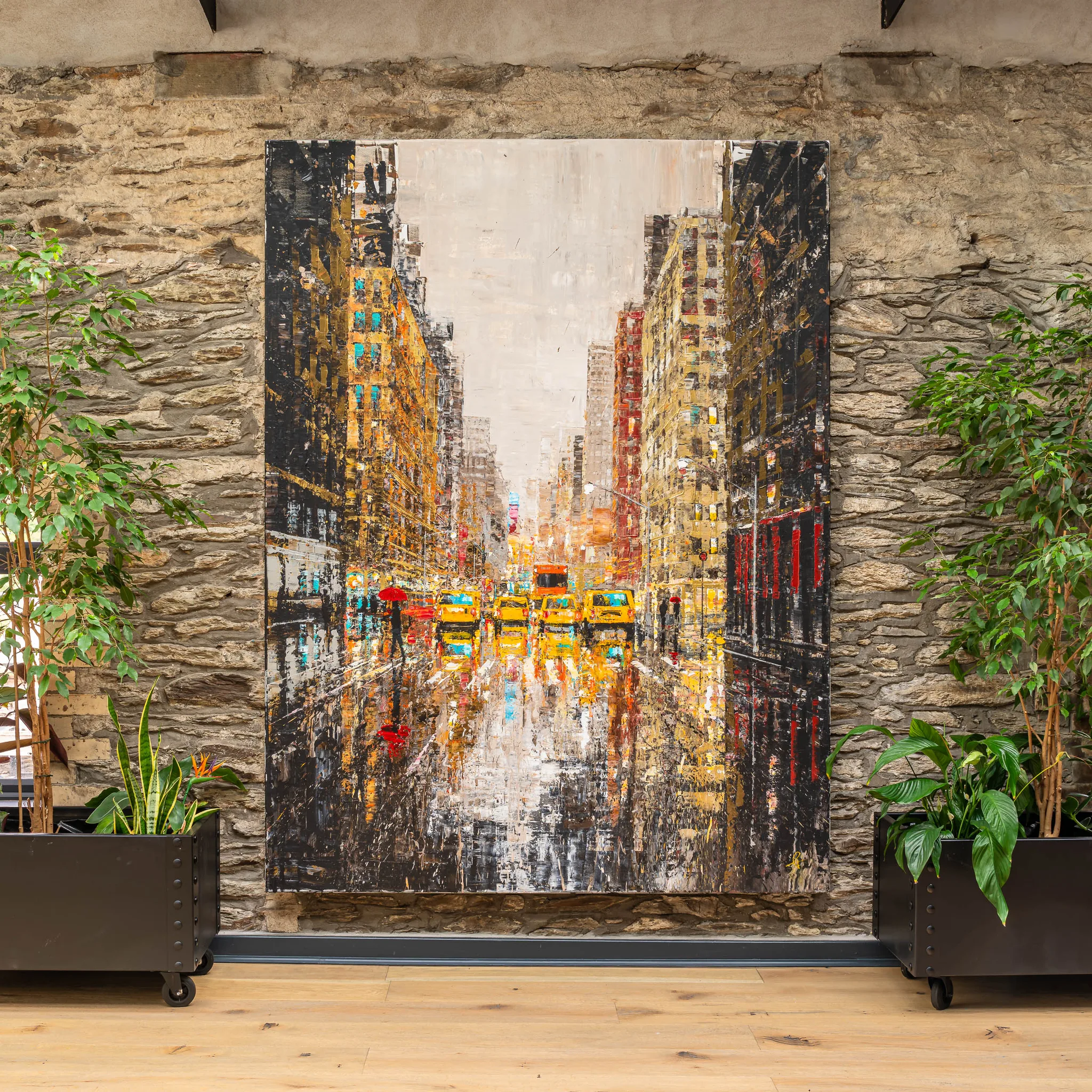 Golden Metropolis, an original painting by Paul Kenton, hangs on a stone wall between potted plants, showing a rain-slicked New York street lined with glowing gold towers and yellow taxis.