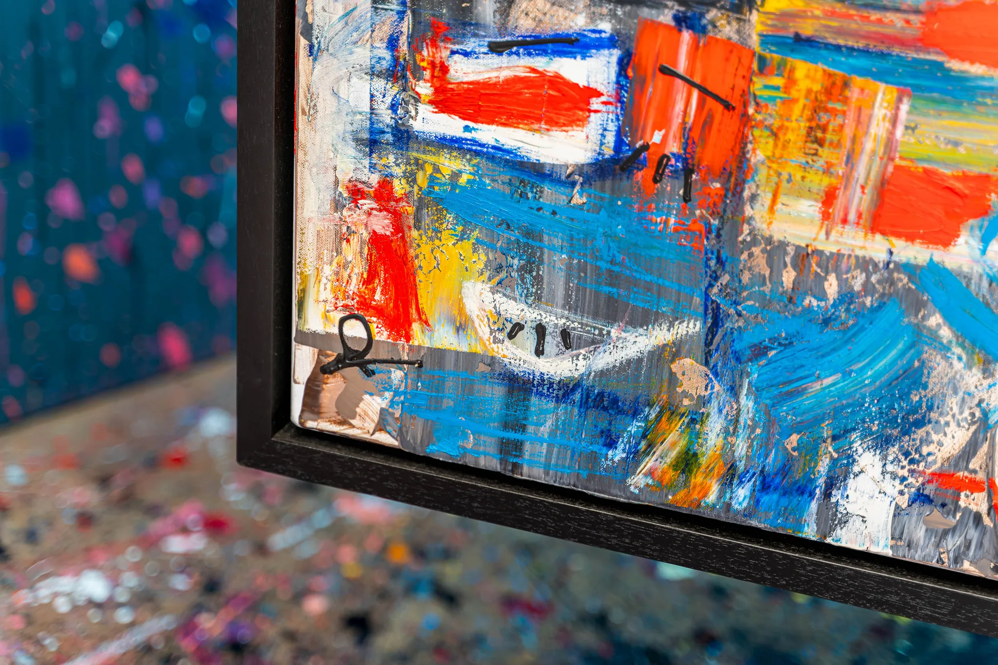 Close-up of Laid Back, an original mixed media painting by Paul Kenton, showing thick red, blue and yellow impasto strokes, scraped texture and a black floating frame edge.