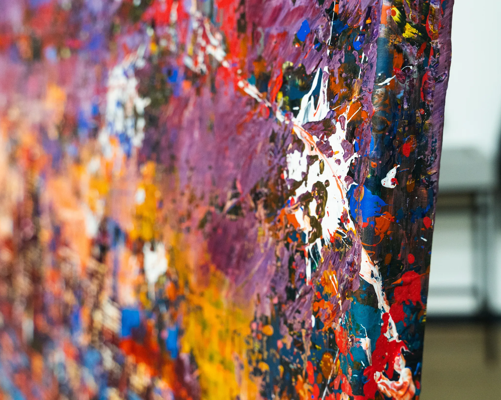 Close-up of London in Motion, an original mixed media painting by Paul Kenton, showing thick, textured layers of purple, orange, red and blue paint with white splashes along the canvas edge.