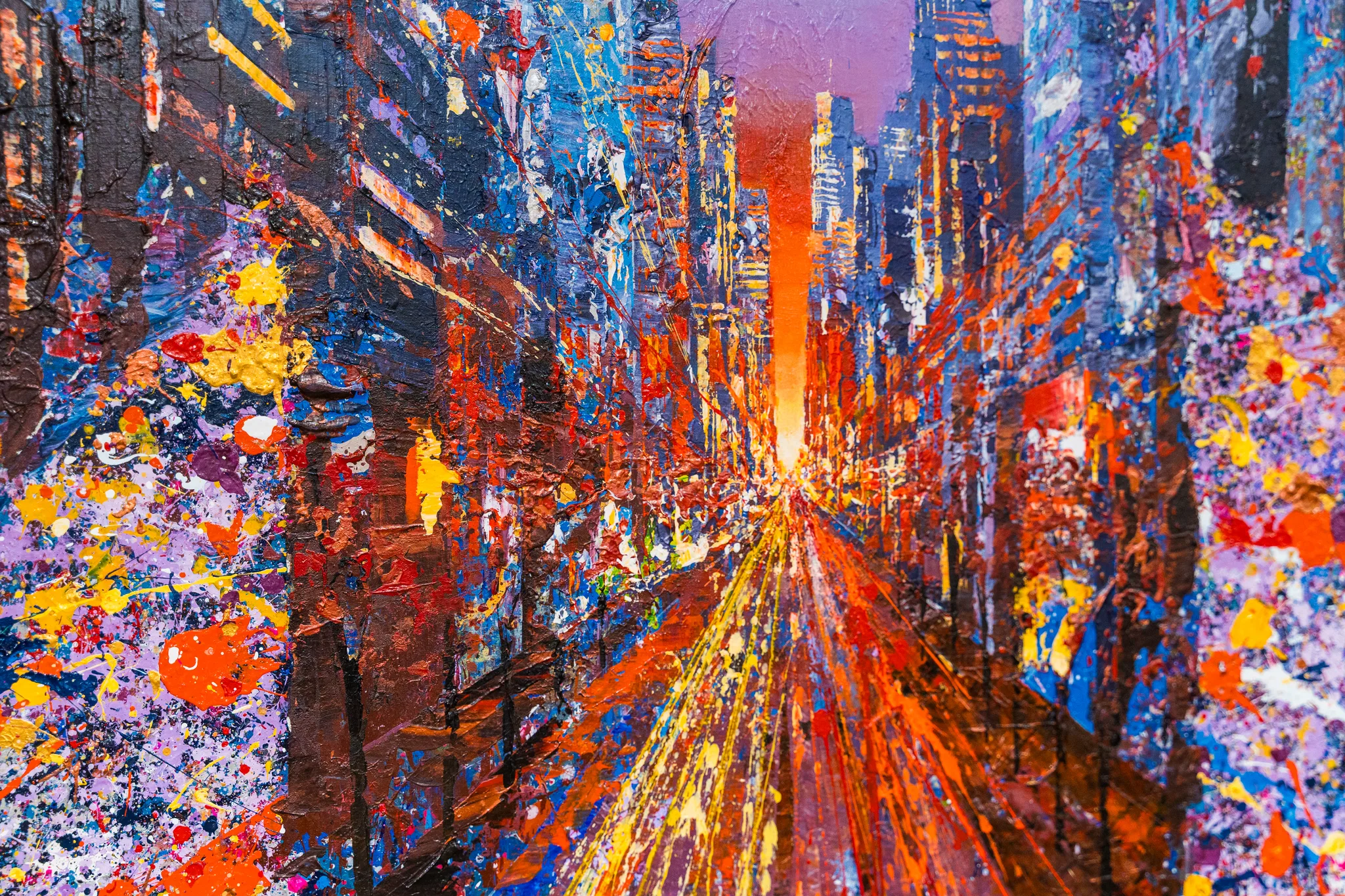 Close-up of Manhattan Burst, an original painting by Paul Kenton: a city avenue glowing orange at dusk, with thick, splattered paint in blue, purple, yellow and red on the towers.
