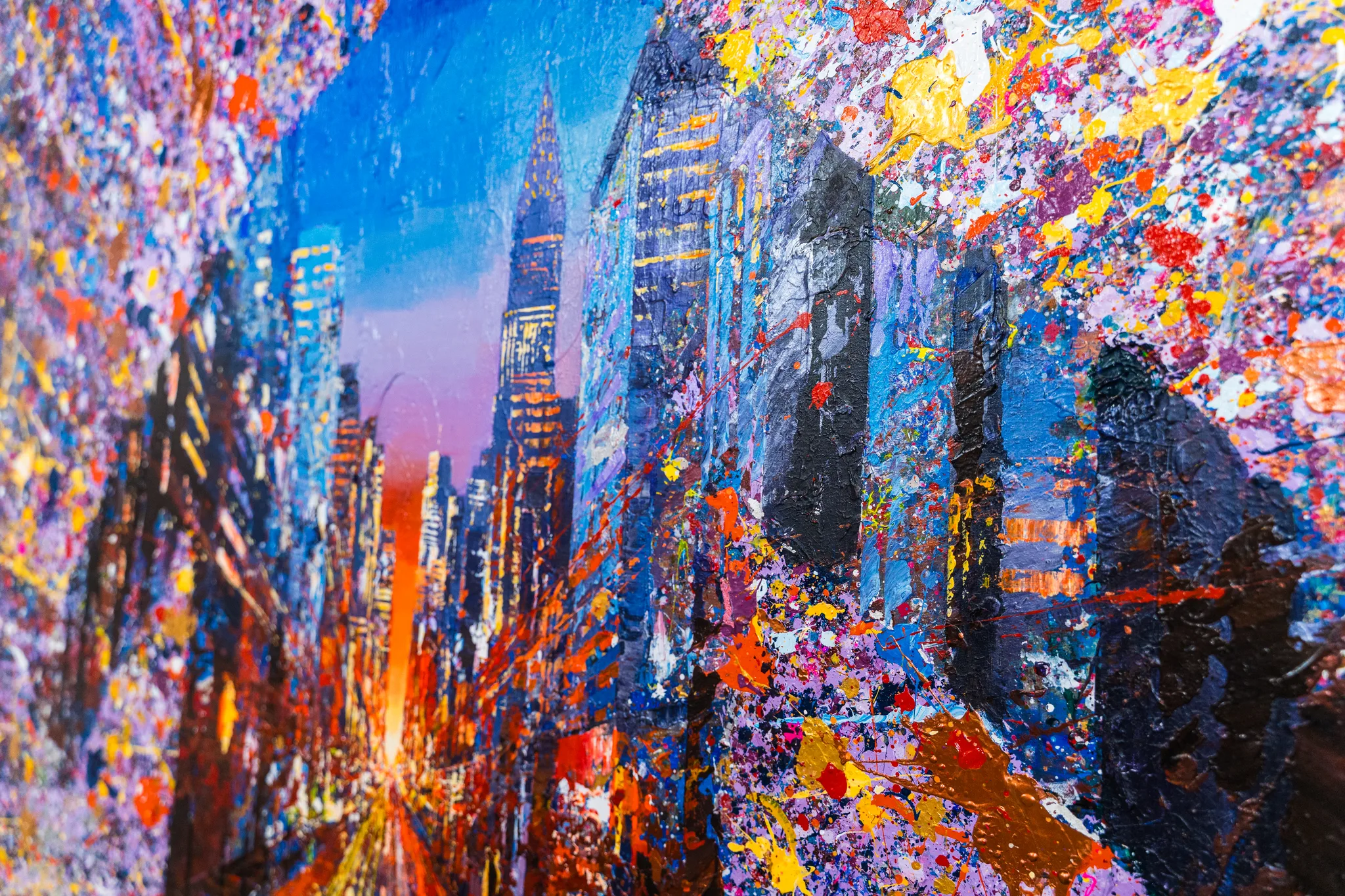 Close-up of Manhattan Burst, an original painting by Paul Kenton: a city street of tall towers under blue dusk, overlaid with bursts of gold, red, violet and orange paint splatter.
