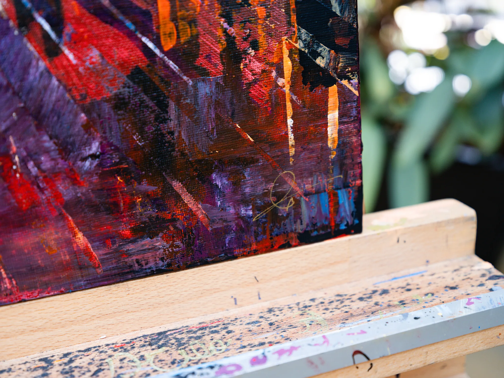 Close-up of Manhattan Heat, an original painting by Paul Kenton, showing thick, textured strokes of red, orange, purple and black with metallic flecks at the lower corner, resting on a wooden easel.