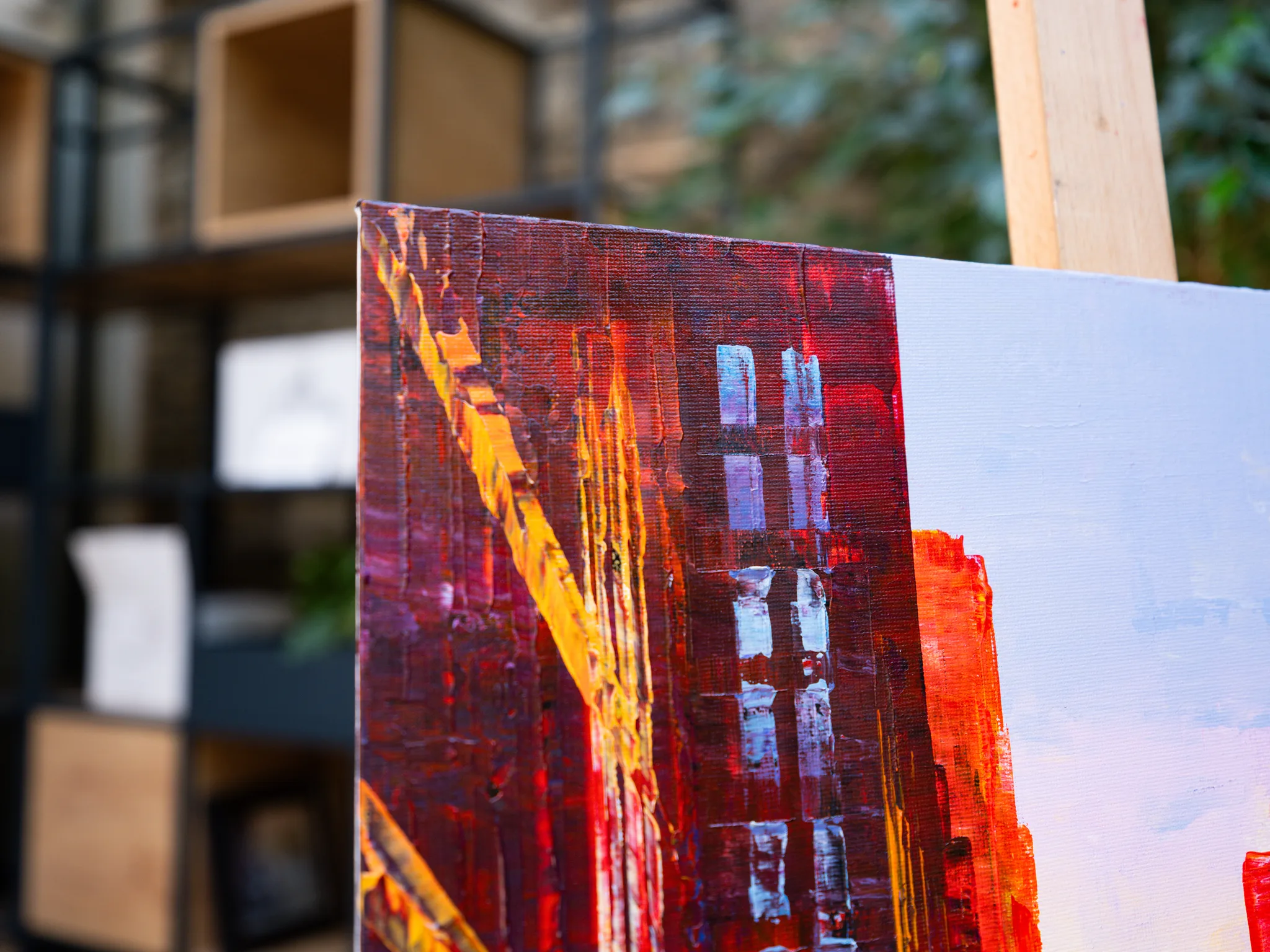 Close-up of Manhattan Heat, an original painting by Paul Kenton: thick, textured red and gold brushstrokes over a dark maroon ground, with pale blue-grey strokes of tower windows and sky at right.