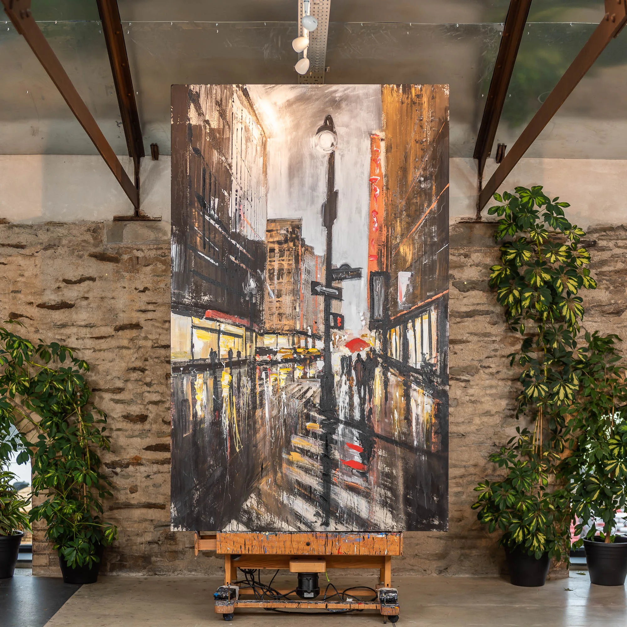 Manhattan Showers: a tall painting of a rain-soaked city street at dusk, with a glowing street lamp, red umbrella and blurred yellow lights reflecting on wet pavement, in warm browns, greys and golds.