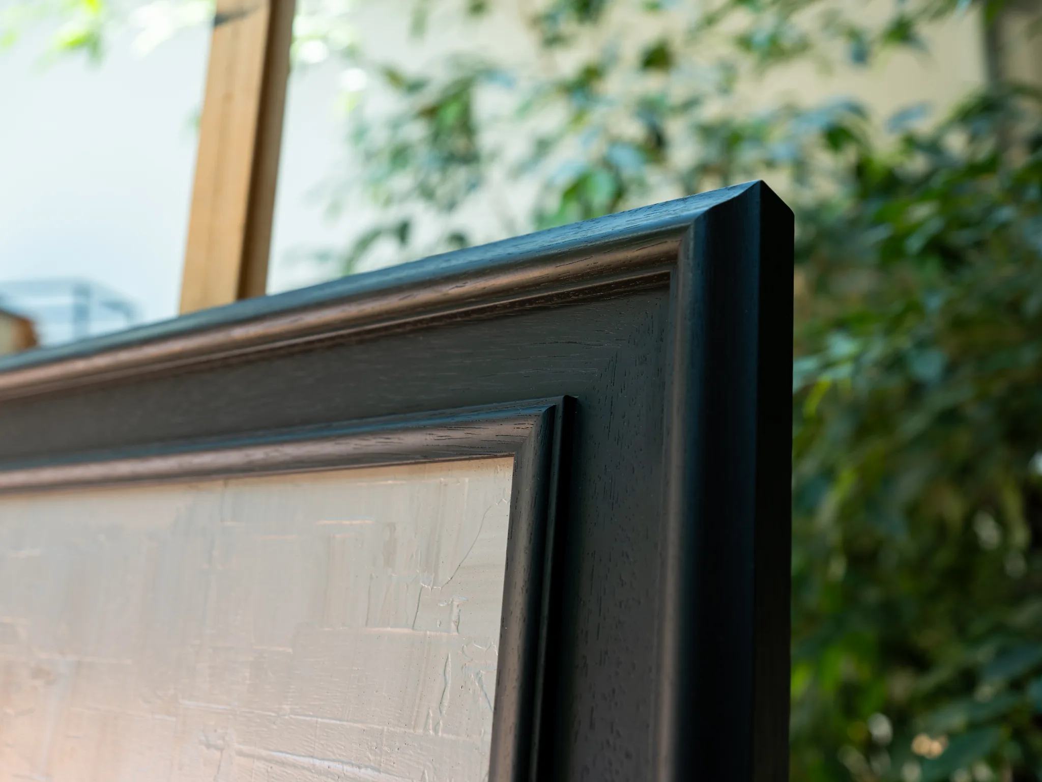 Close-up of the dark wooden frame corner around Midtown Silver, showing the pale, textured silver paint surface beneath it.