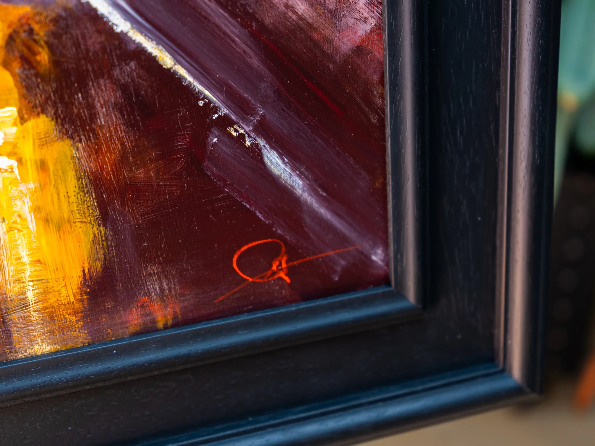 Close-up of Night Drive, an original mixed media painting by Paul Kenton, showing thick dark maroon brushstrokes, glints of gold and a bright orange signature in the lower corner, within a black frame.