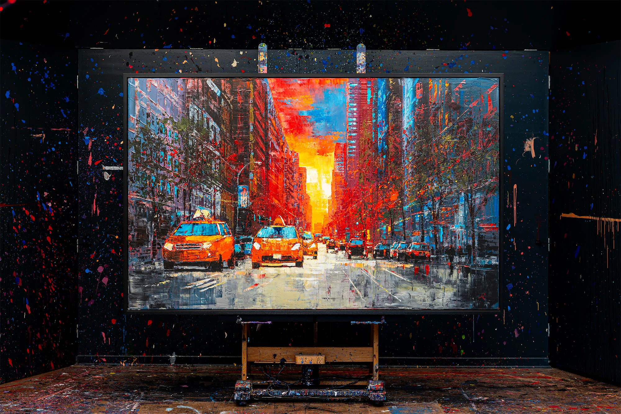 NY Ablaze, an original mixed media painting by Paul Kenton, shown on an easel in a paint-splattered studio. A city street glows with fiery orange sunset light between yellow taxis.