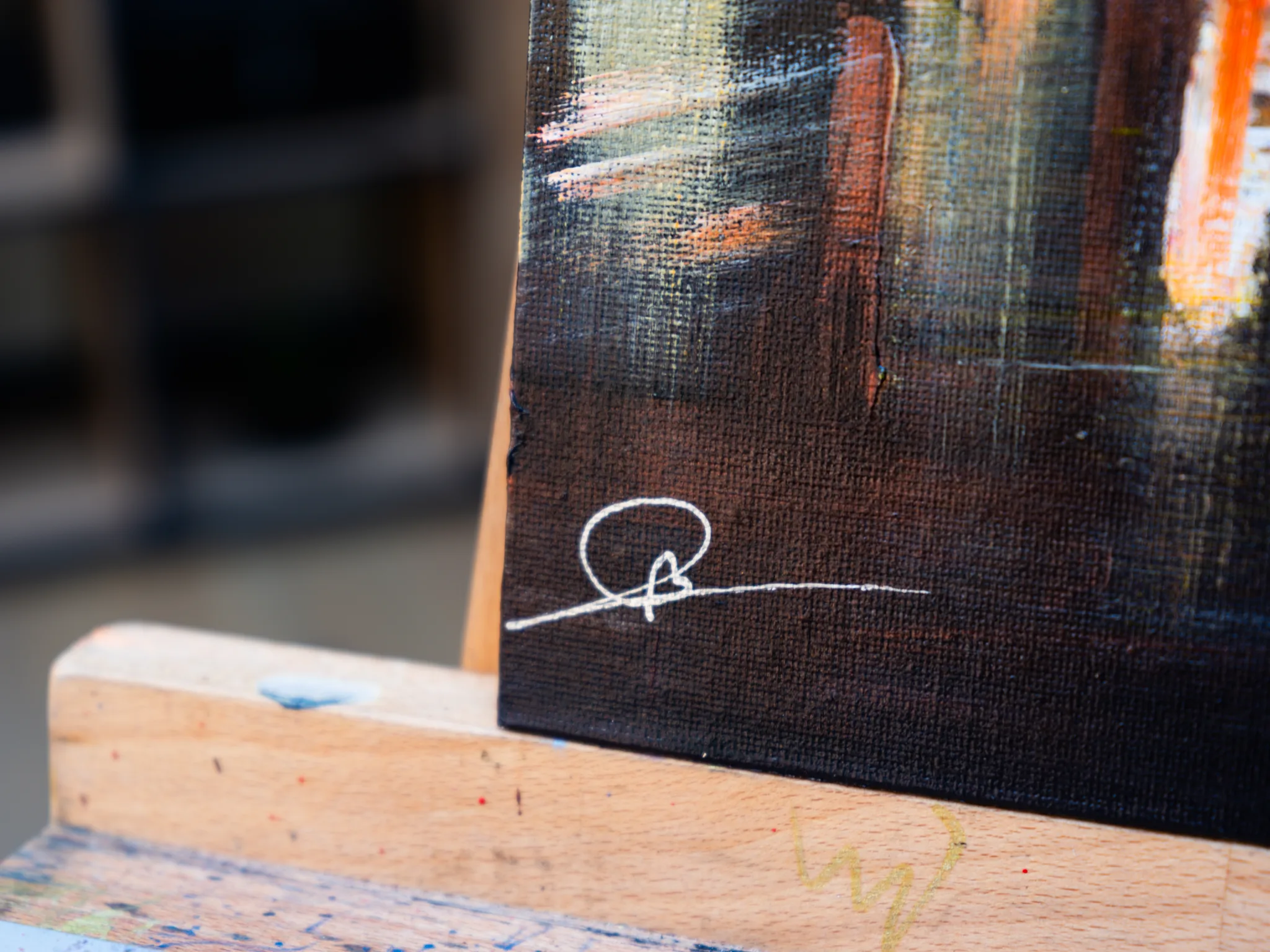 Close-up of the lower corner of Under the Chrysler, an original painting by Paul Kenton, showing a white signature over dark textured paint with streaks of orange and pale light.