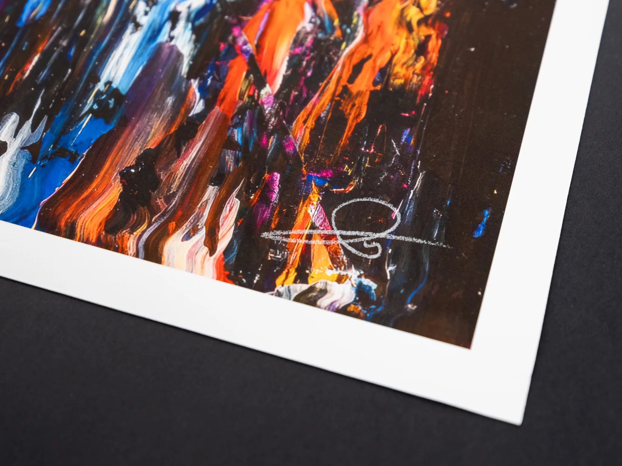 Close-up of a corner of the Downtown Dazzle limited edition giclée print, showing bold orange, blue and violet brushstrokes over dark night-time city tones, with a white pencil signature on the lower right and a white paper margin.