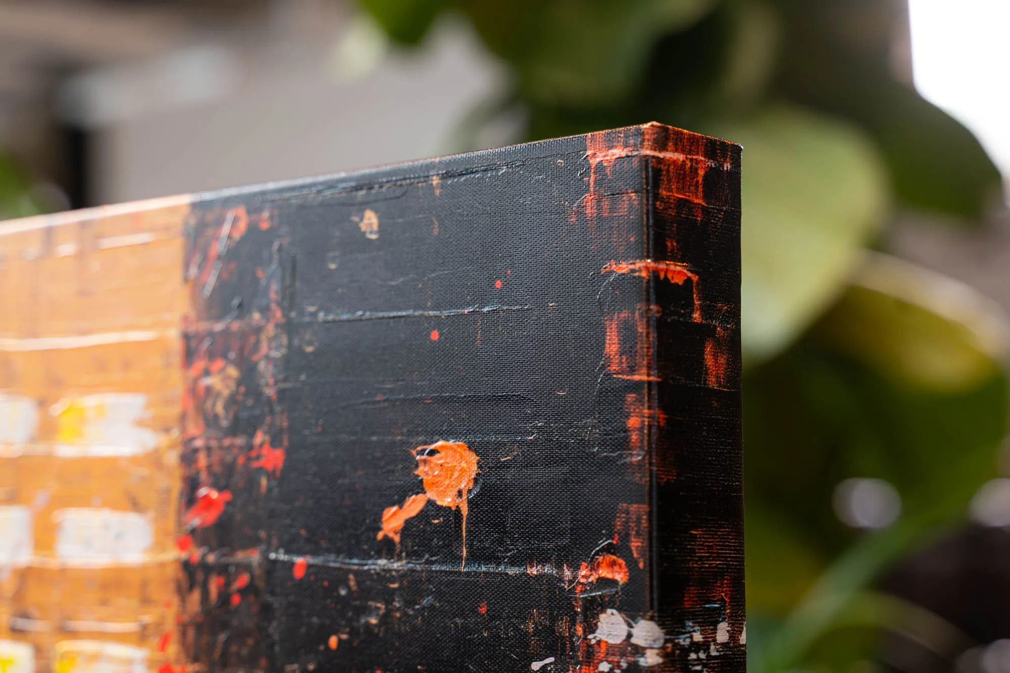 Close-up of the side edge of Downtown Reflections, an embellished giclée print on boxed canvas, showing black paint with orange drips and streaks and a golden panel with white marks.