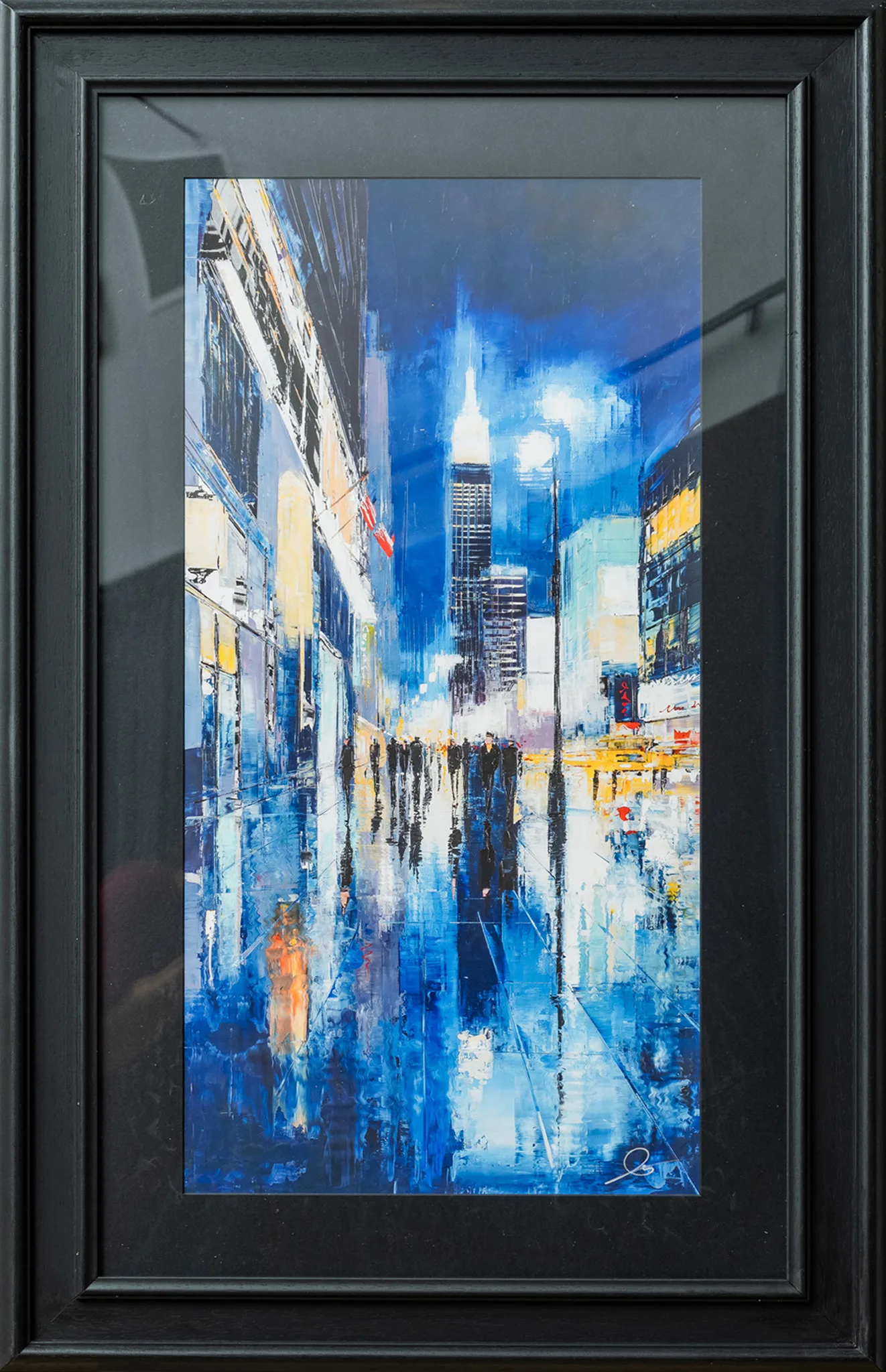 Electric City, a night-time New York street scene in blue tones, with wet reflective pavement, glowing lights, and a lit skyscraper spire rising above figures in the distance. The print sits in a slim black frame with a wide dark mat.