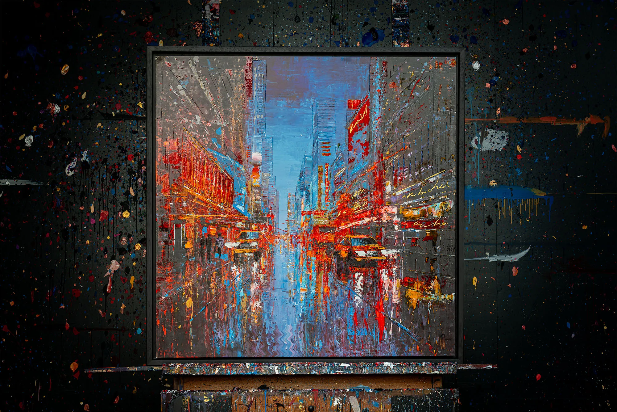 Empire City Spectrum: a vibrant, textured cityscape of a busy street at dusk, with red and orange neon glows against cool blue skies and reflective greys. Shown framed on a dark, paint-splattered wall.
