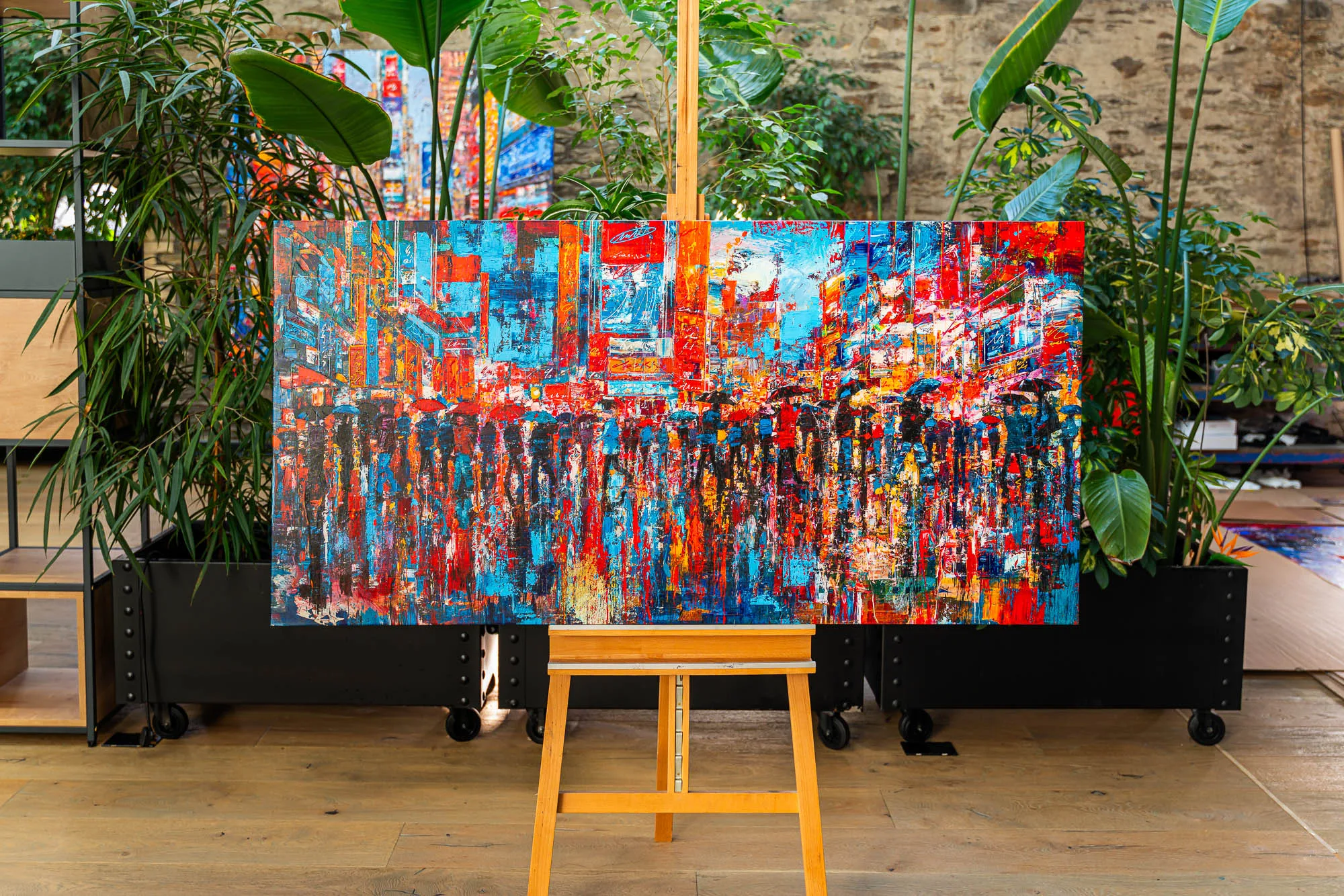 Fairytale Of New York, a limited edition embellished giclée print on boxed canvas by Paul Kenton, on an easel among potted plants. Bold red, blue and cyan neon streaks evoke a rain-soaked New York street at night.