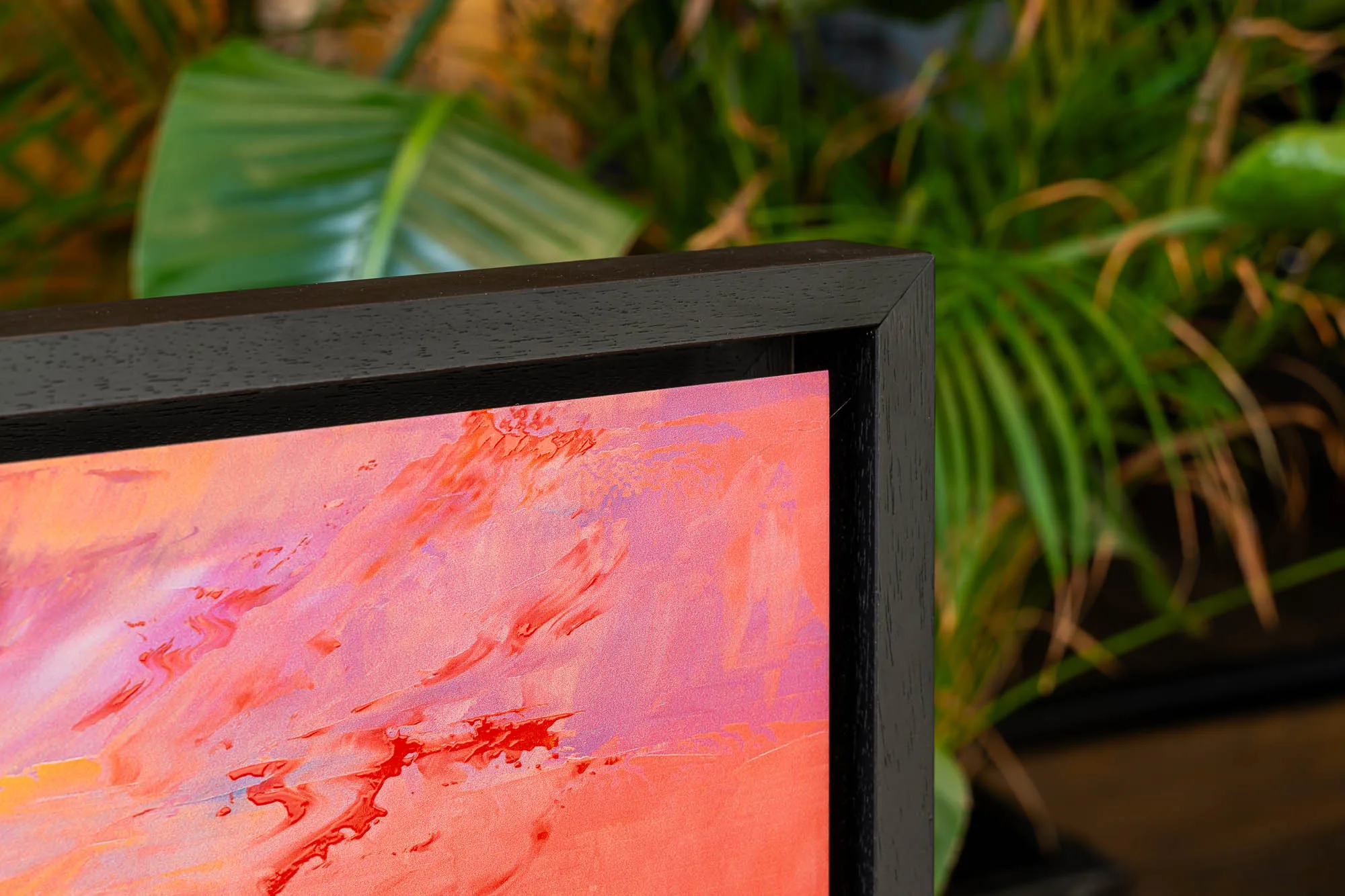Close-up of London Ablaze, a limited edition print by Paul Kenton, showing a corner of its black frame and swirling red, orange and pink textured brushwork against green foliage.