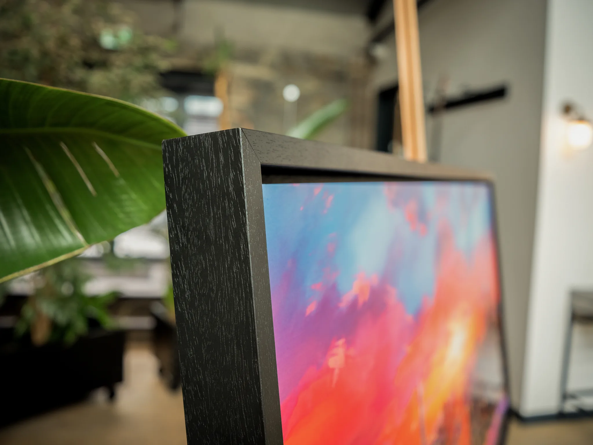 Close-up of London Embers, a limited edition print by Paul Kenton, showing a black textured frame edge and bold blue, pink and orange brushwork blazing beside a leafy plant.