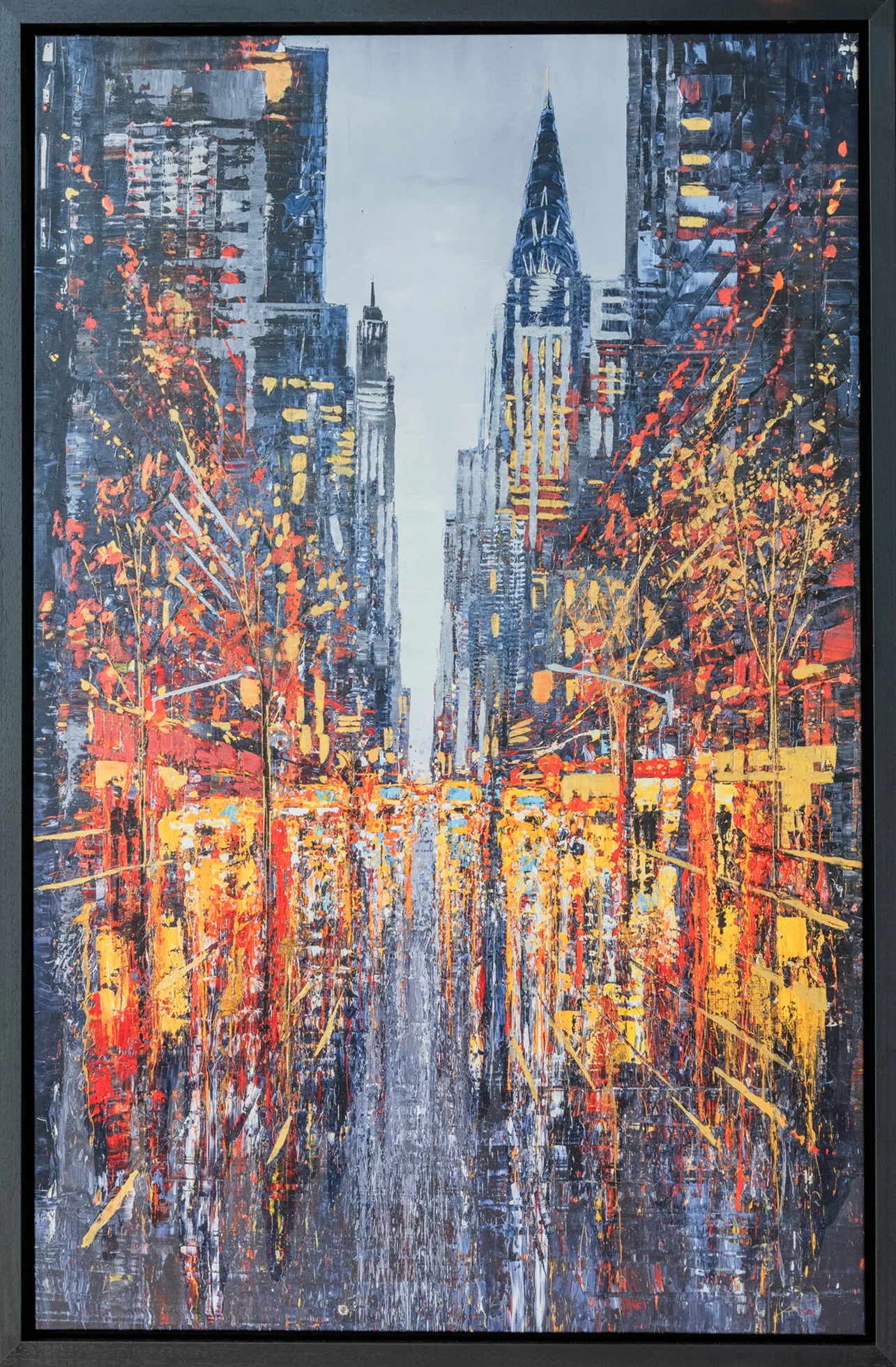 New York Serenade, an embellished giclée print in a slim black float frame: a rain-slicked avenue of tall grey towers, with a spire rising at centre, and warm orange and red lights and textured brushwork glowing along the street.