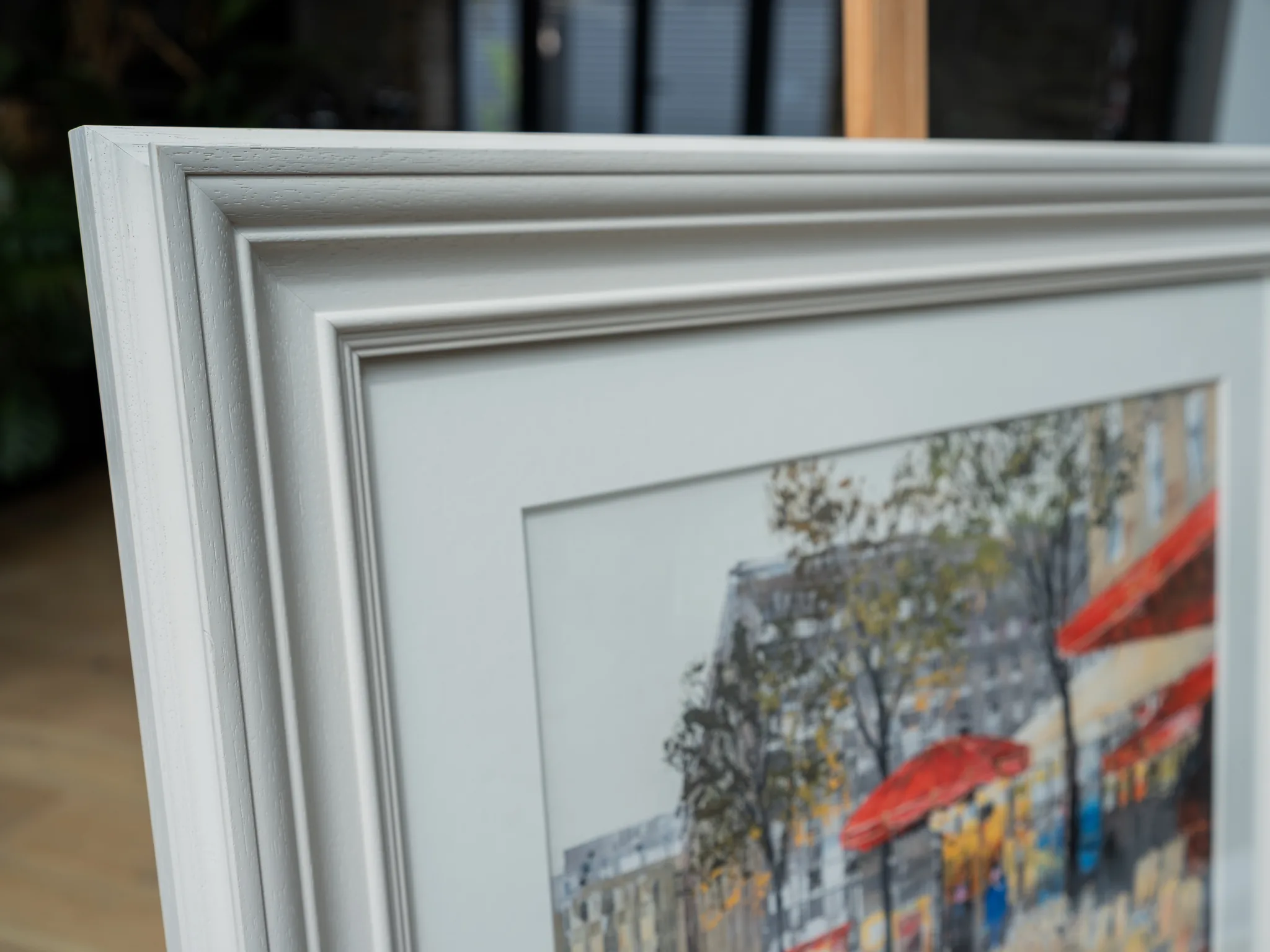 Parisien Life, a limited edition giclée print by Paul Kenton, framed in a pale grey moulded frame with a cream mount, showing a Paris street with red awnings and parasols.