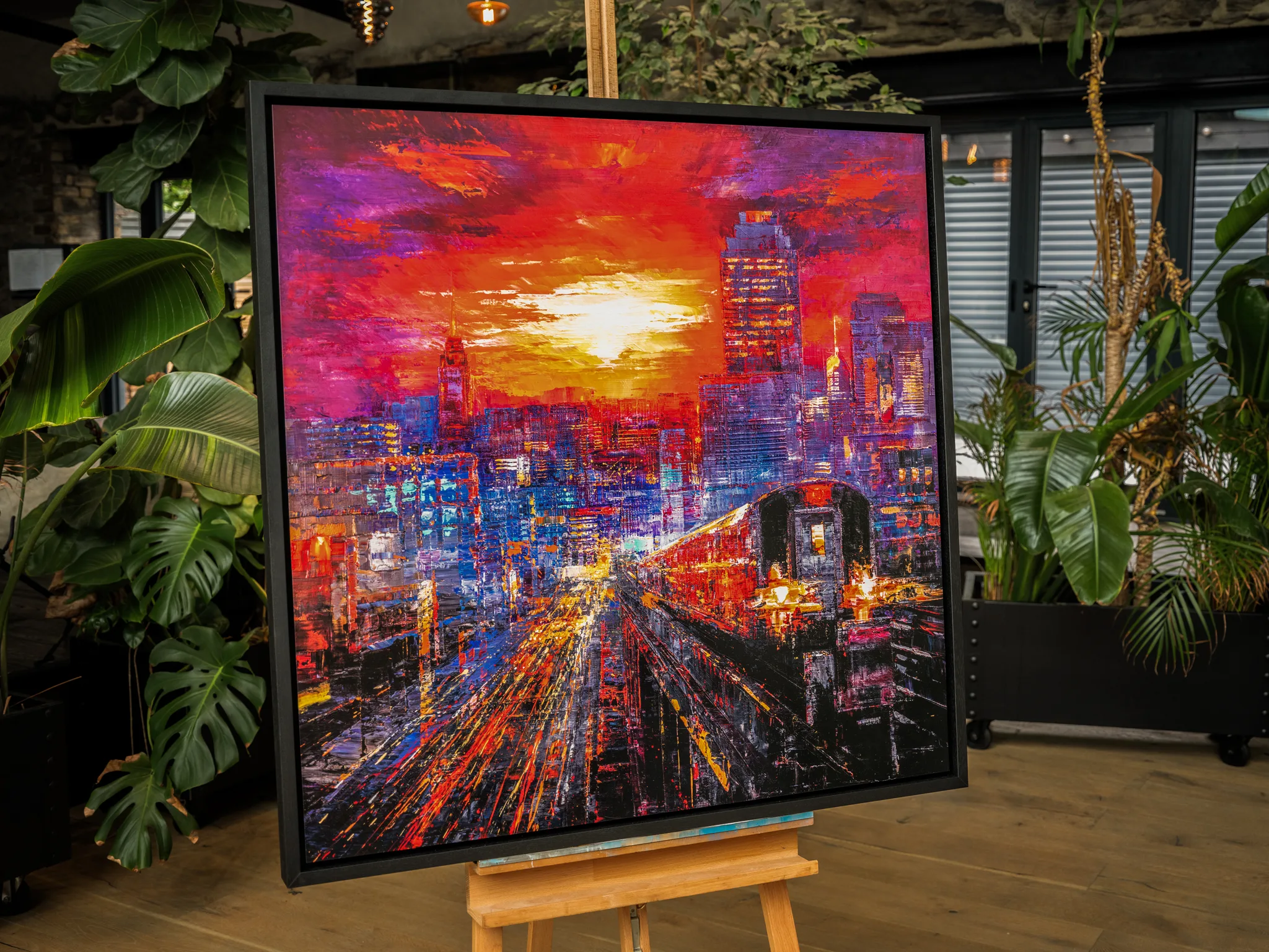 Urban Approach, a limited edition print by Paul Kenton, on an easel: a fiery sunset over a New York skyline and train.