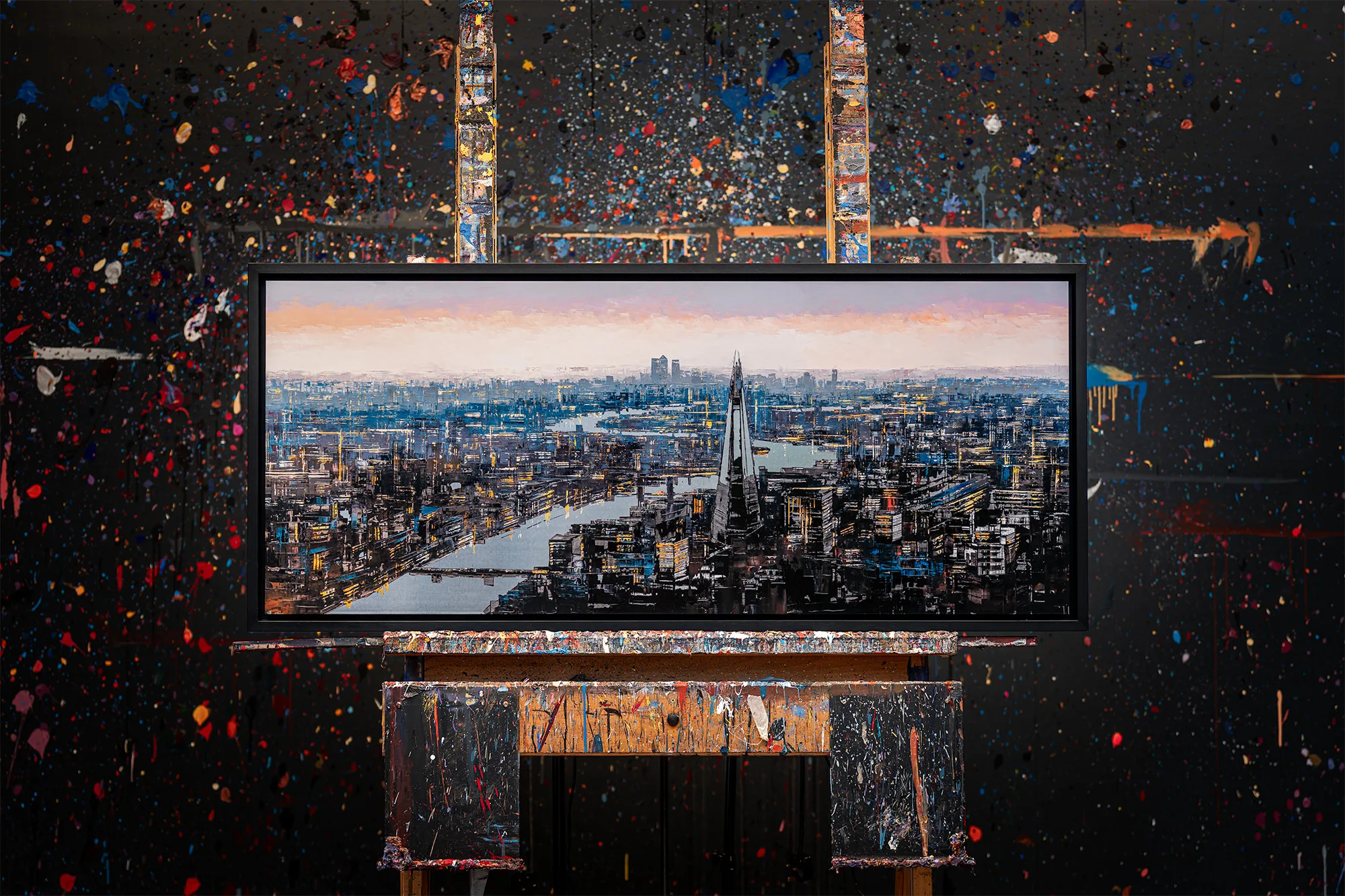 Vista Reflections, a limited edition print by Paul Kenton, hangs framed above a paint-splattered table in a studio, showing a textured London skyline at dusk with the Shard and the Thames.