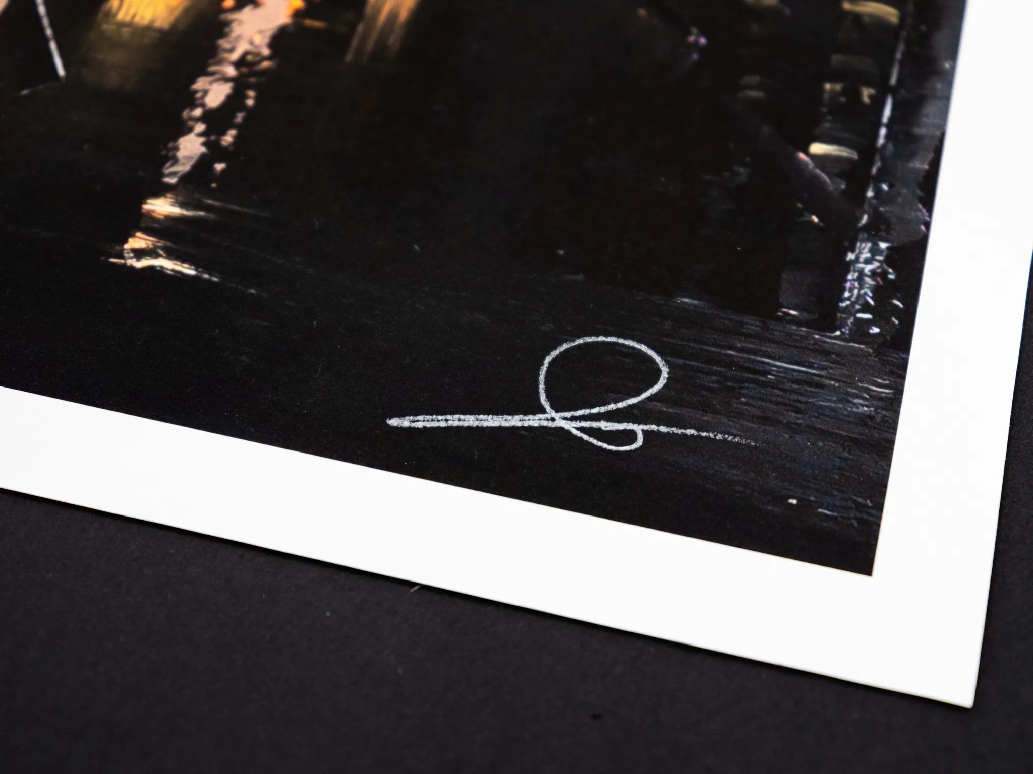 Close-up of the lower corner of Manhattan Glow, a limited edition giclée print, showing dark textured paint with warm amber city lights and a white hand-signed signature.