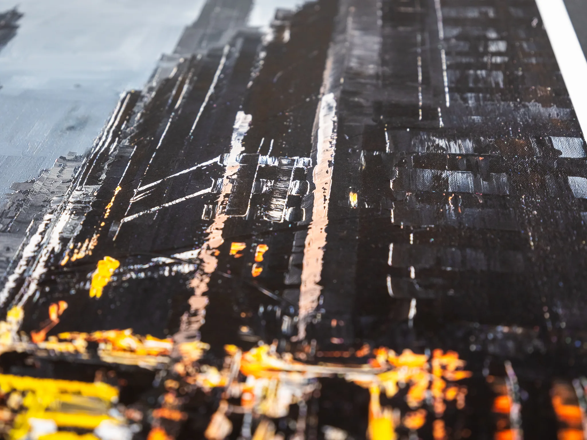 Close-up of the textured surface of Manhattan Glow, a limited edition print, showing dark towers of thick impasto with pale streaks and glowing yellow and orange paint at the base.