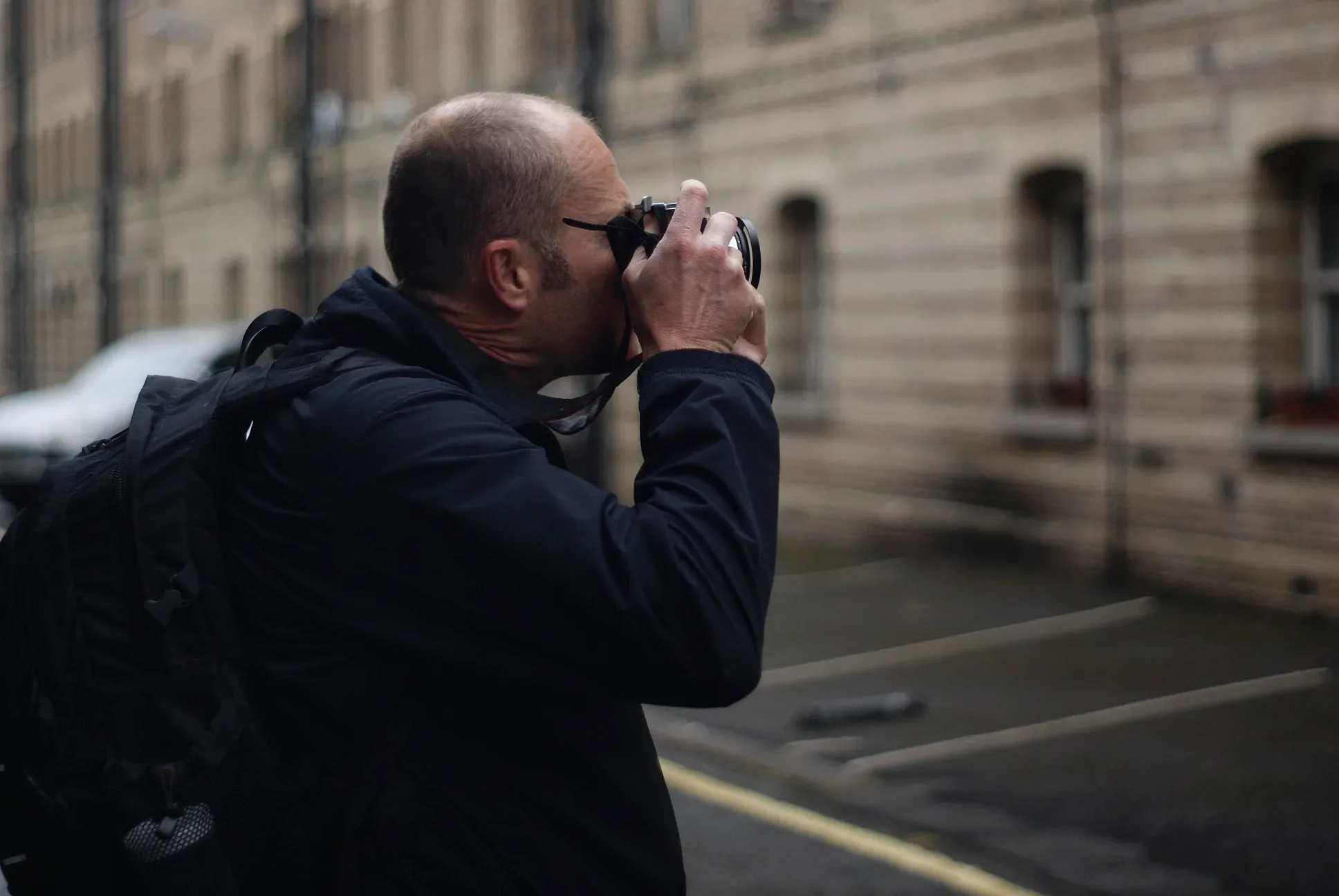 Paul Kenton, a rucksack on his back, raising a camera to photograph a street of stone buildings