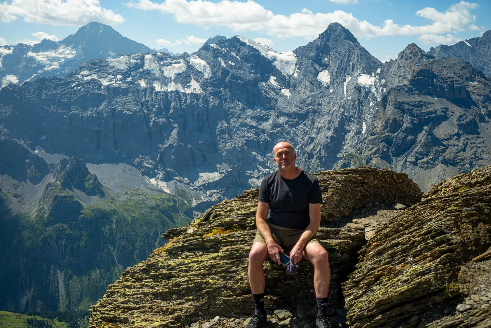 Paul Kenton sitting on a mossy rock outcrop, steep grey mountains and glaciers behind him
