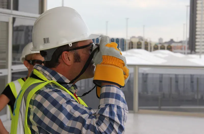 Paul Kenton in a hard hat and high-visibility vest standing beside London Glory on a balcony, with the real Olympic Stadium behind him