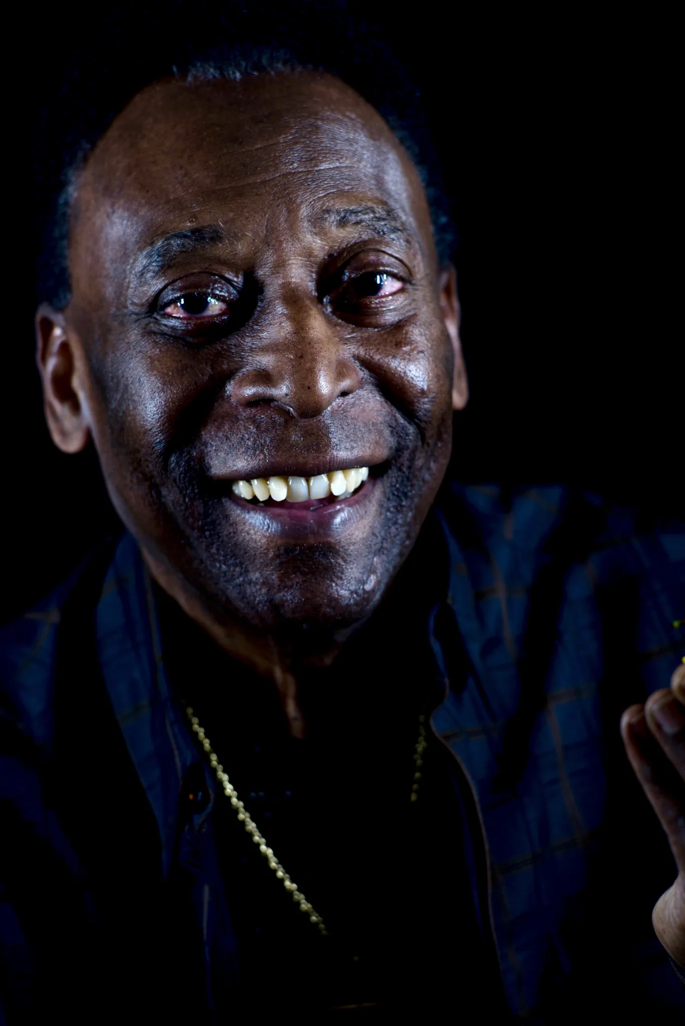 Portrait of Pelé smiling warmly at the camera, lit from the side against a black background
