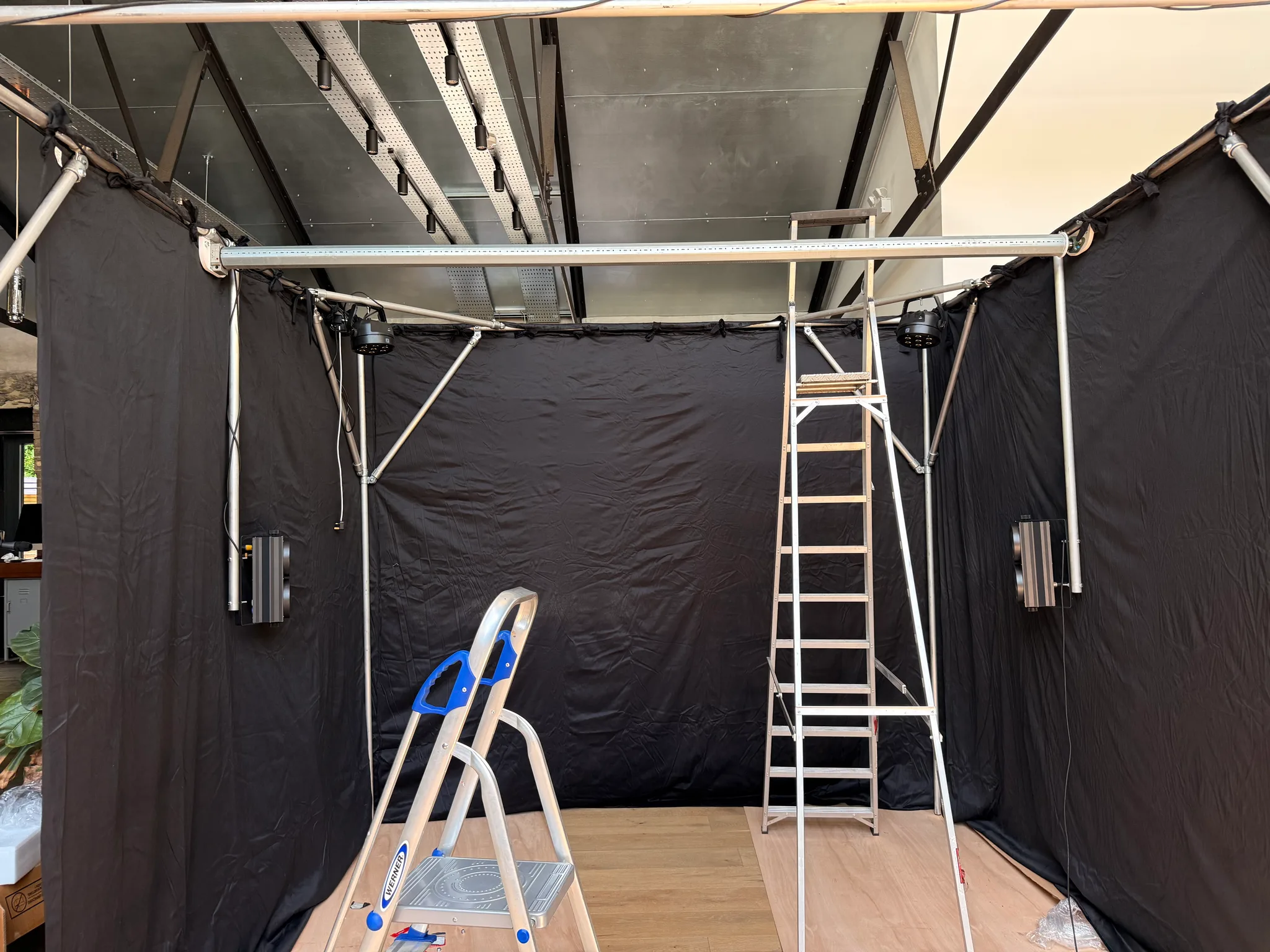 Looking across the black-draped room, a steel rail runs along the top bar, with fittings mounted on either side and two ladders on the timber floor.