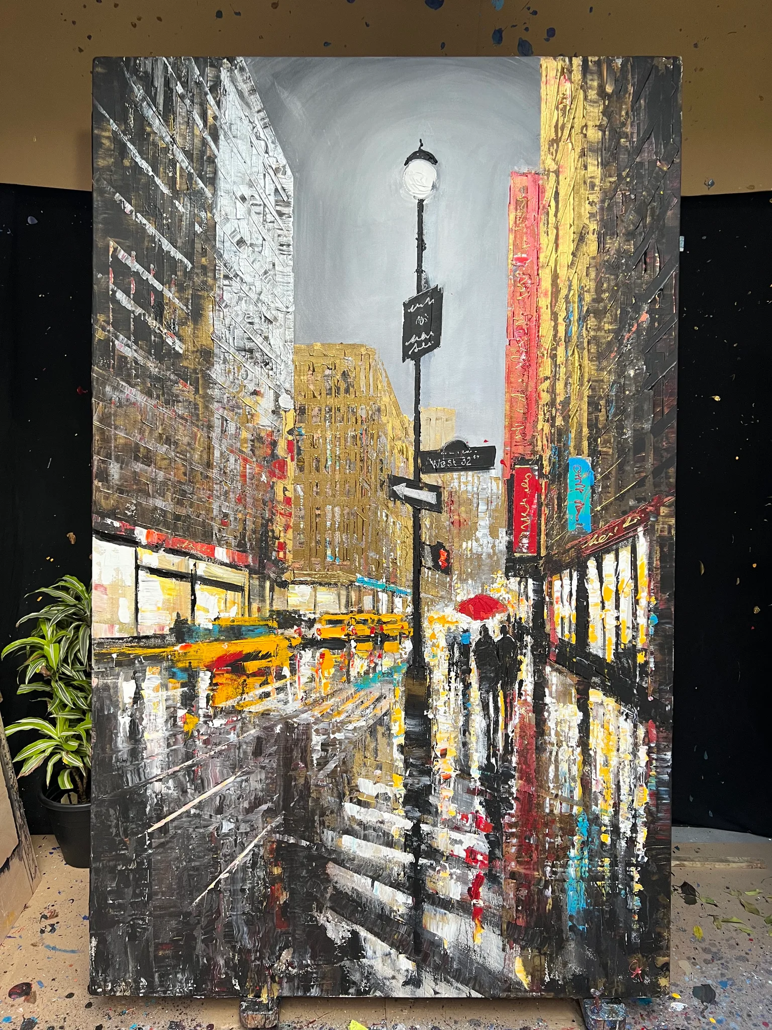 Manhattan Showers, an original painting by Paul Kenton shown in a studio: a rain-soaked New York street at dusk, with yellow taxis, a red umbrella and figures crossing, in bold textured grey, gold and red.