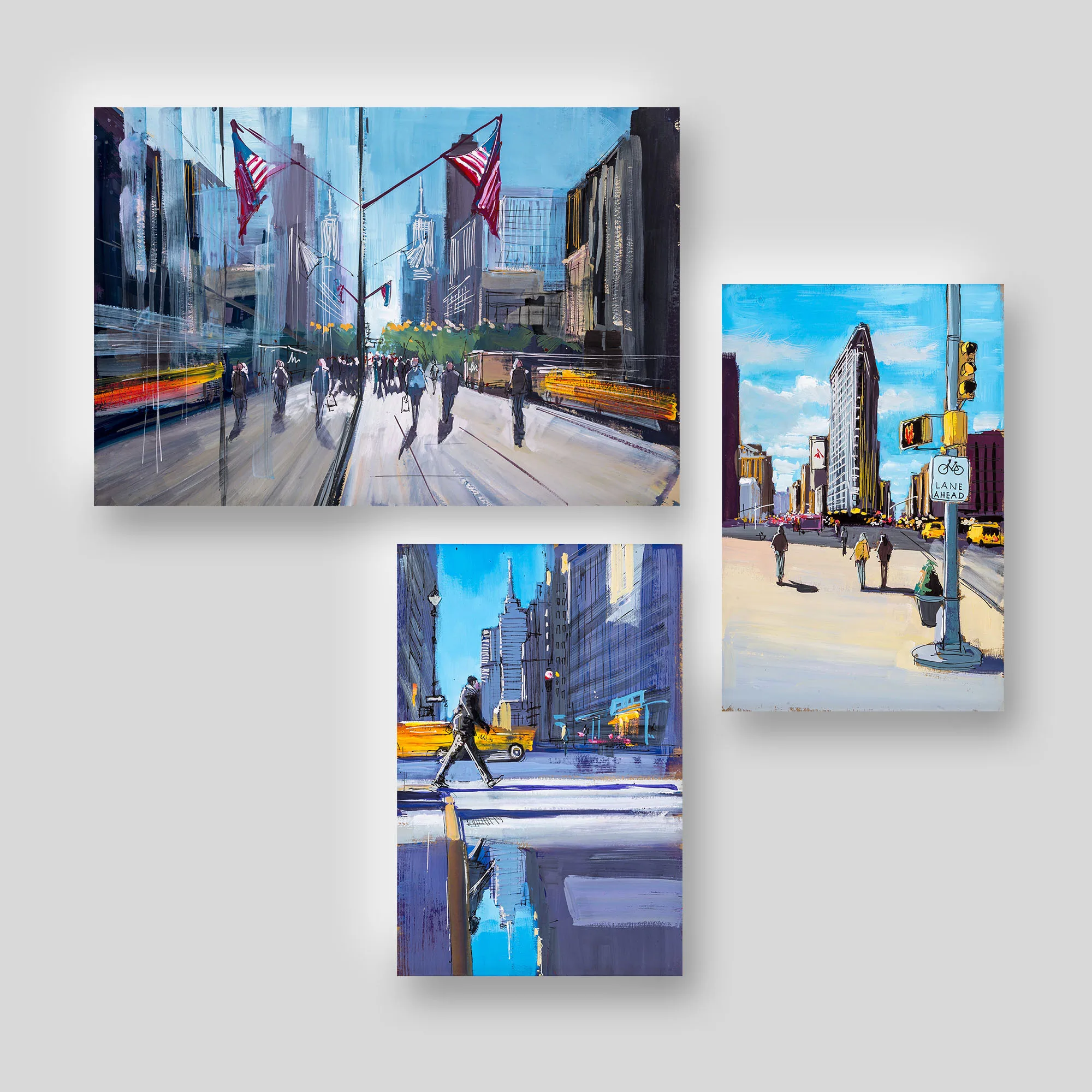 Streets of New York I, a print collection set by Paul Kenton: three New York street scenes, with a large central view of American flags over a busy avenue, the Flatiron Building on a sunny corner, and a lone pedestrian crossing a blue-toned street.