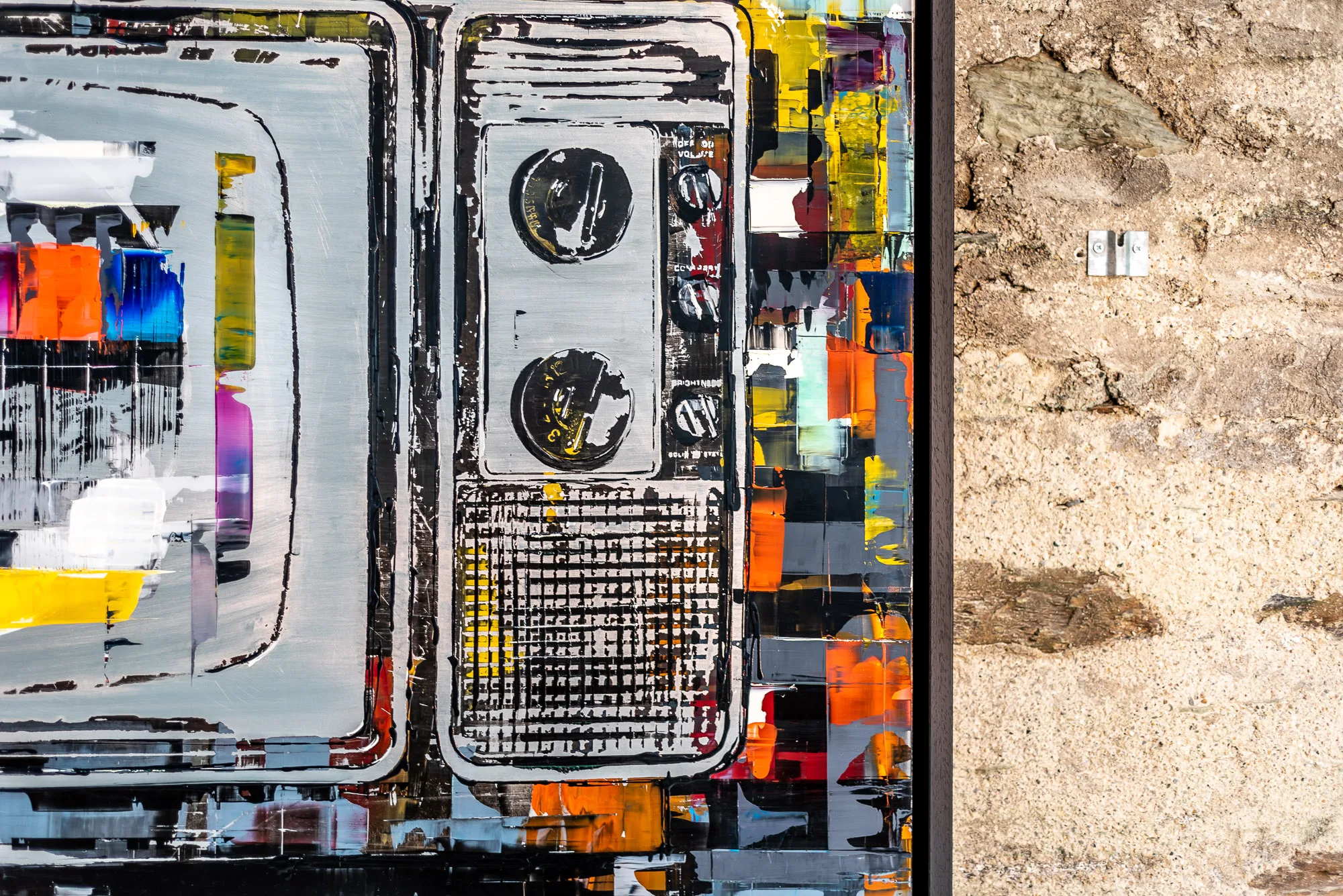 Close-up of Test Card TV, an original mixed media painting on aluminium by Paul Kenton, showing a grey television-like form with two black circles, bold orange, blue and yellow blocks, and gritty black textures.