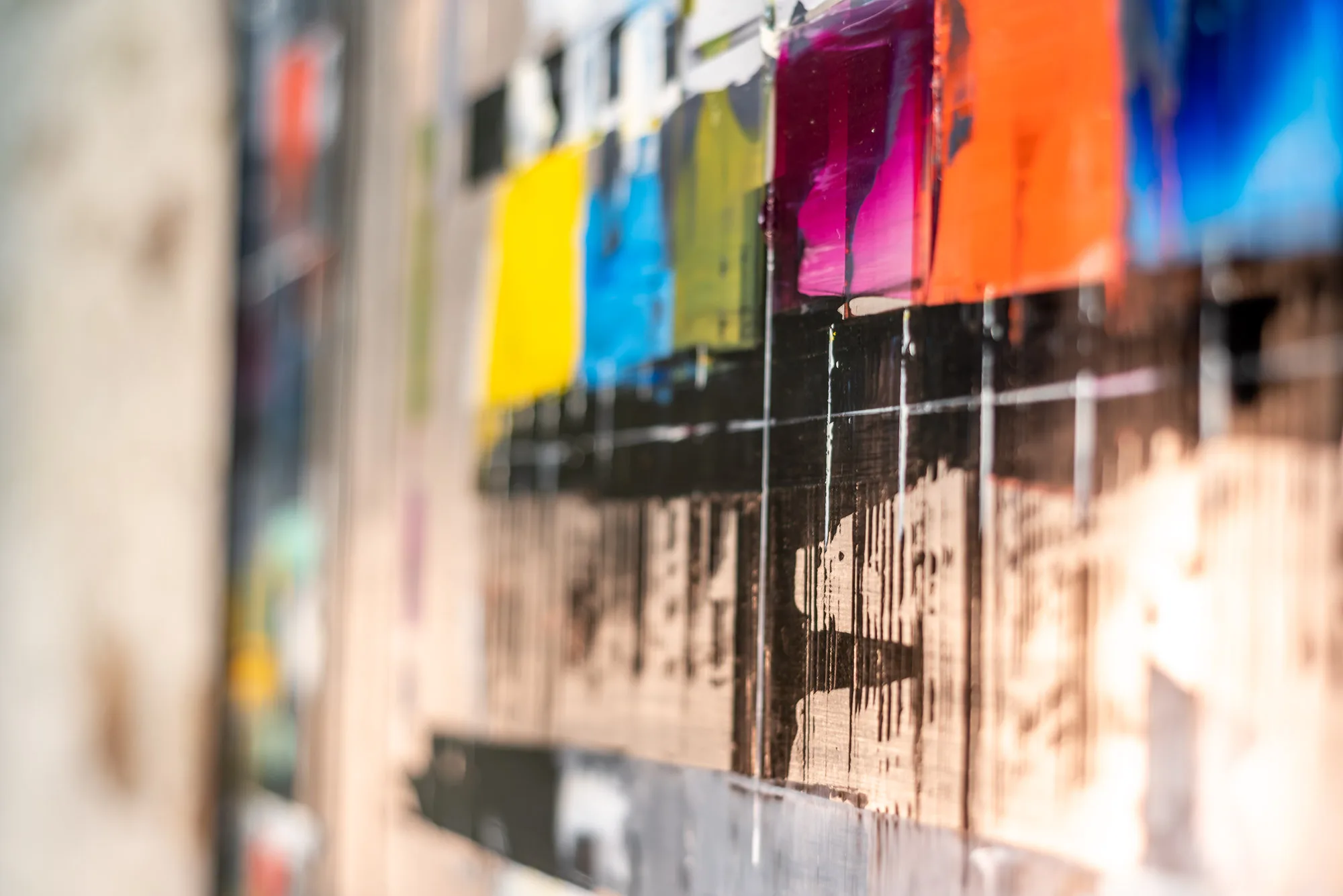 Close-up of Test Card TV, an original mixed-media painting by Paul Kenton on aluminium, showing bold yellow, blue, magenta and orange blocks with dark drips running down a black grid.