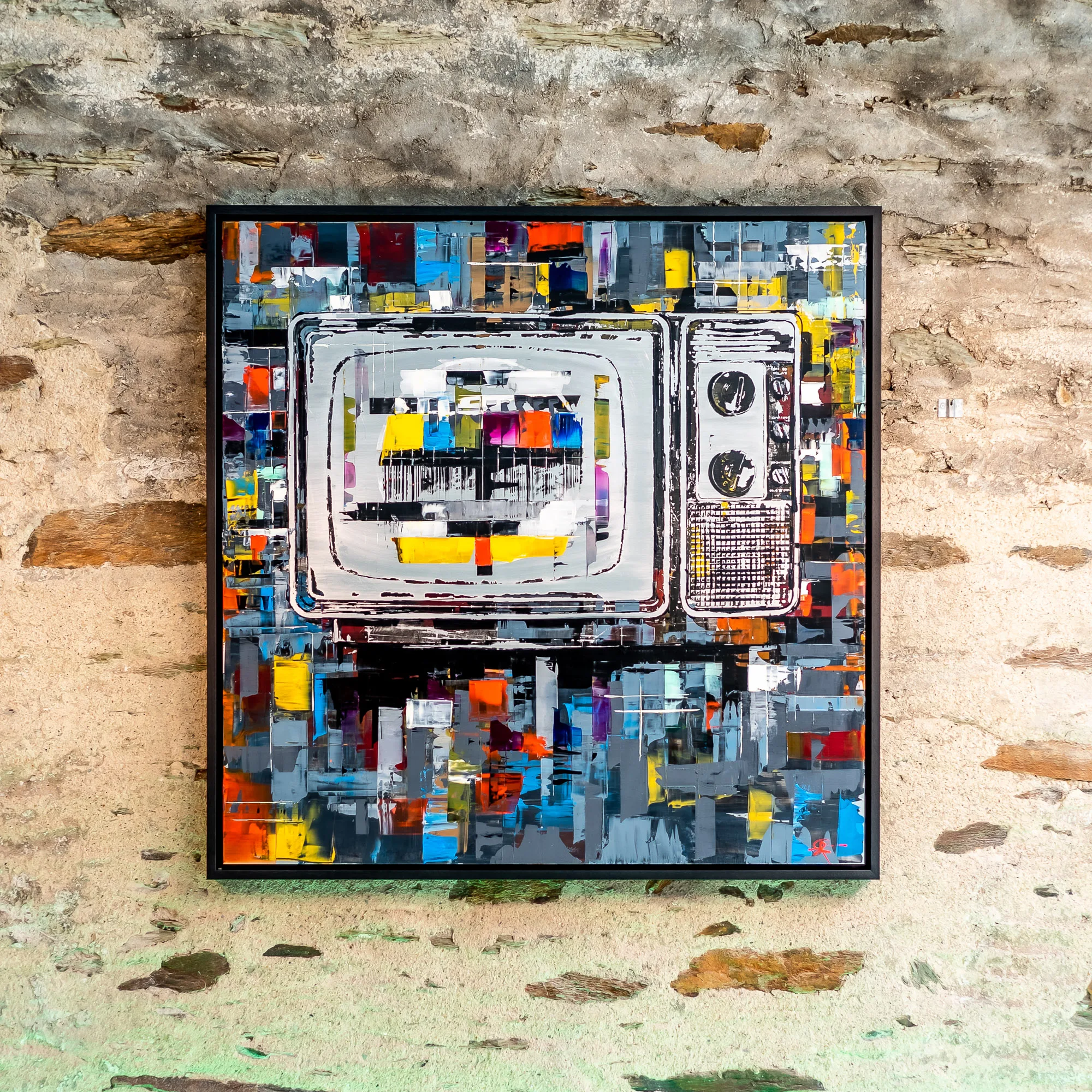 Test Card TV, an original painting by Paul Kenton, hangs in a black frame on a weathered stone wall. A vintage television with a test card glows in grey and white, surrounded by bold blocks of orange, yellow, red and blue.