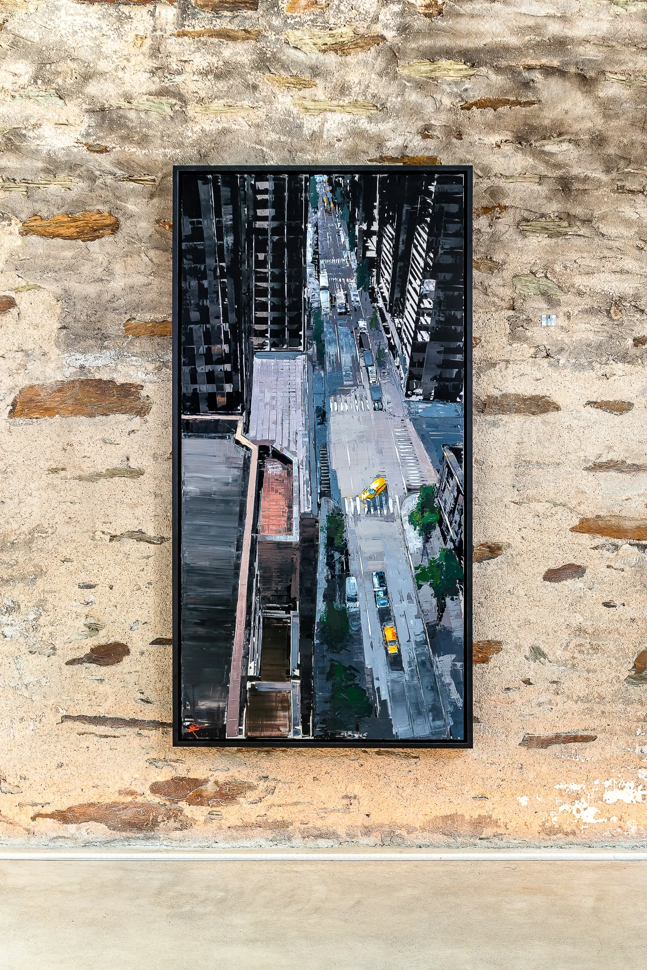 Towering Perspective, an original painting by Paul Kenton hung on a rough stone wall: a tall, bird's-eye view down a New York street between dark towers, with yellow taxis in grey and black tones.