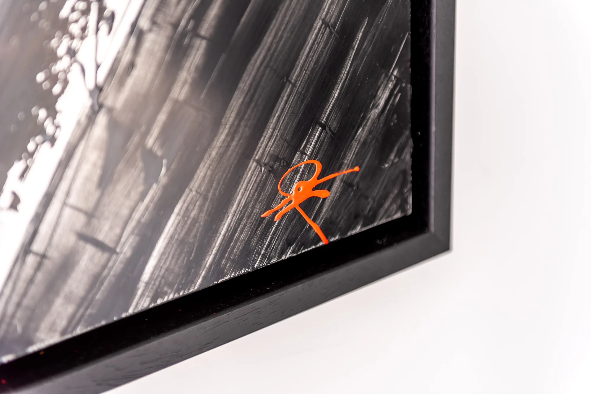 Corner of Start with the Checklist, a black and white mixed media painting on aluminium in a slim black frame, with a loose orange scribble in the lower right.