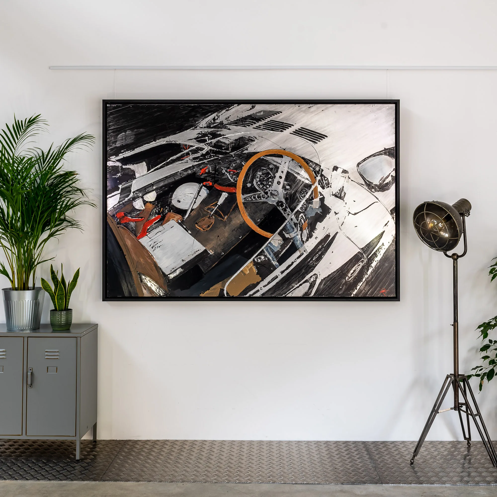 Start with the Checklist, an original mixed media painting by Paul Kenton hanging in a black frame on a white wall, showing a white sports car's cockpit with an orange steering wheel and red accents, beside a grey cabinet and industrial lamp.