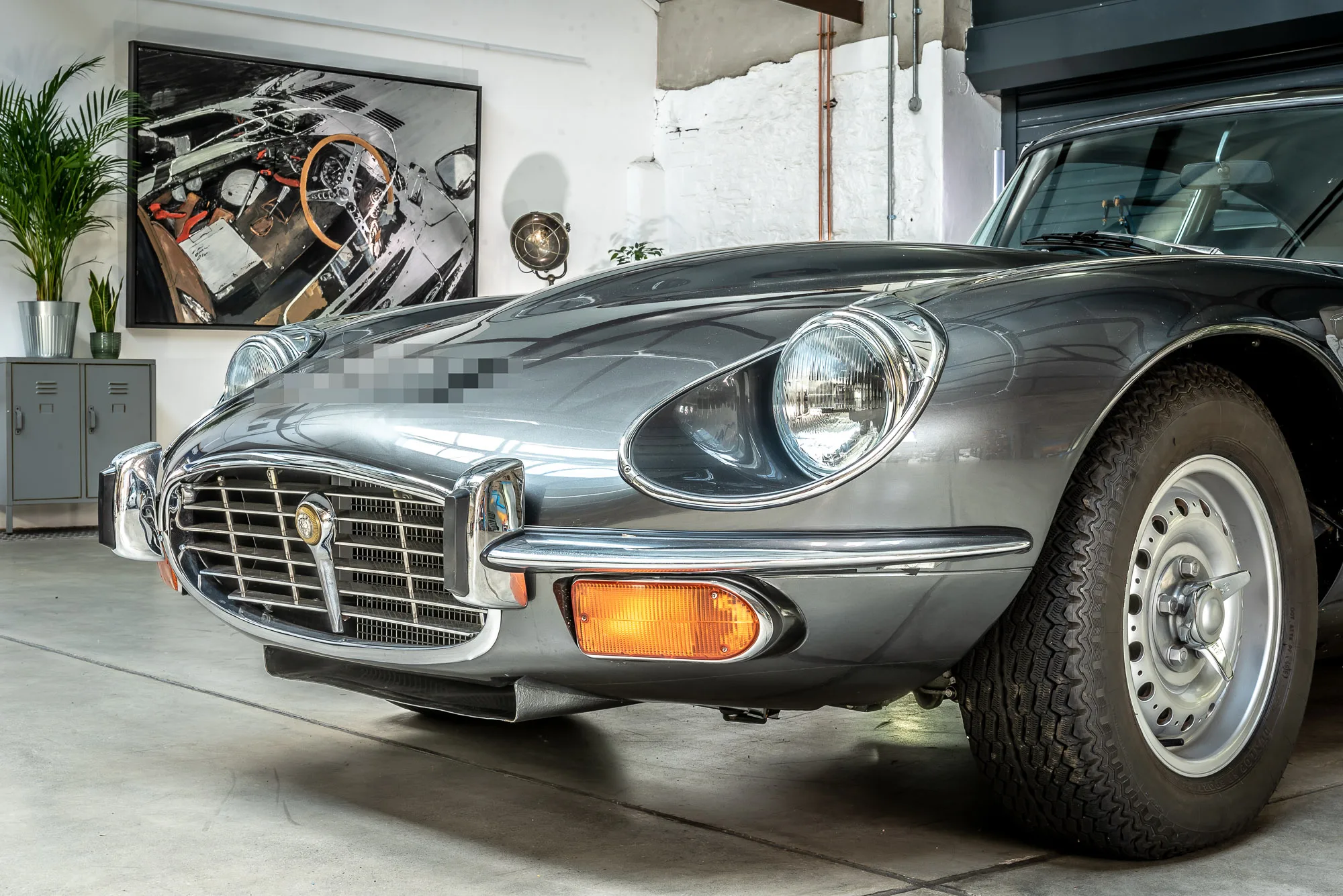 Start with the Checklist, an original mixed media painting on aluminium by Paul Kenton, hangs in a bright studio above a grey classic sports car, with a potted palm beside it.